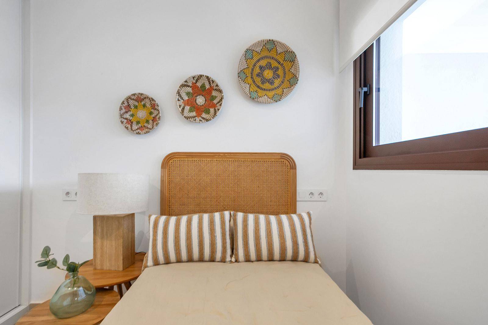 Helles Schlafzimmer mit Einzelbett, Rattan-Kopfteil und farbenfrohen Wanddekorationen.