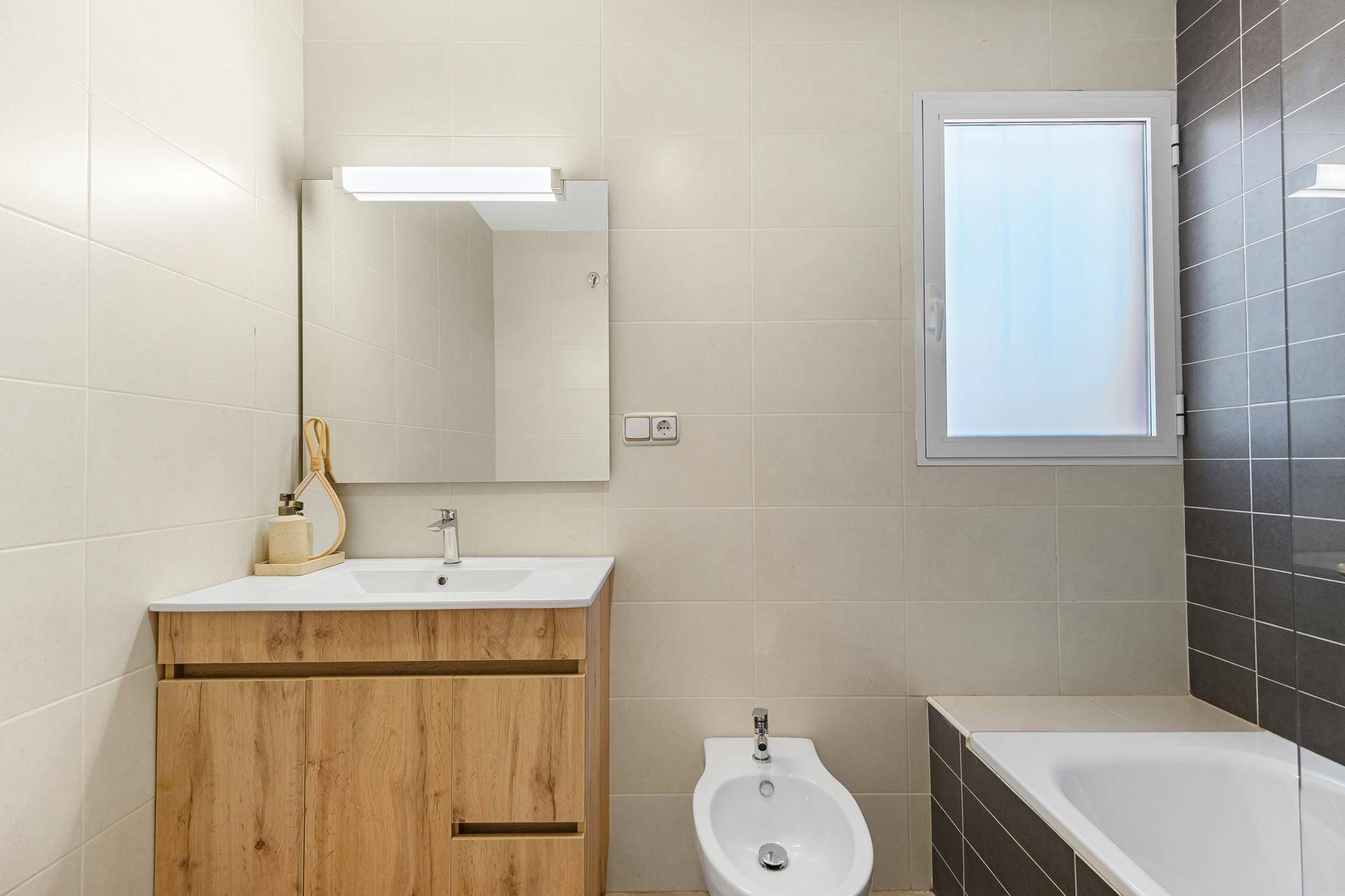 Helles Badezimmer mit Bidet, Badewanne, Holzwaschtisch und großem Spiegel.