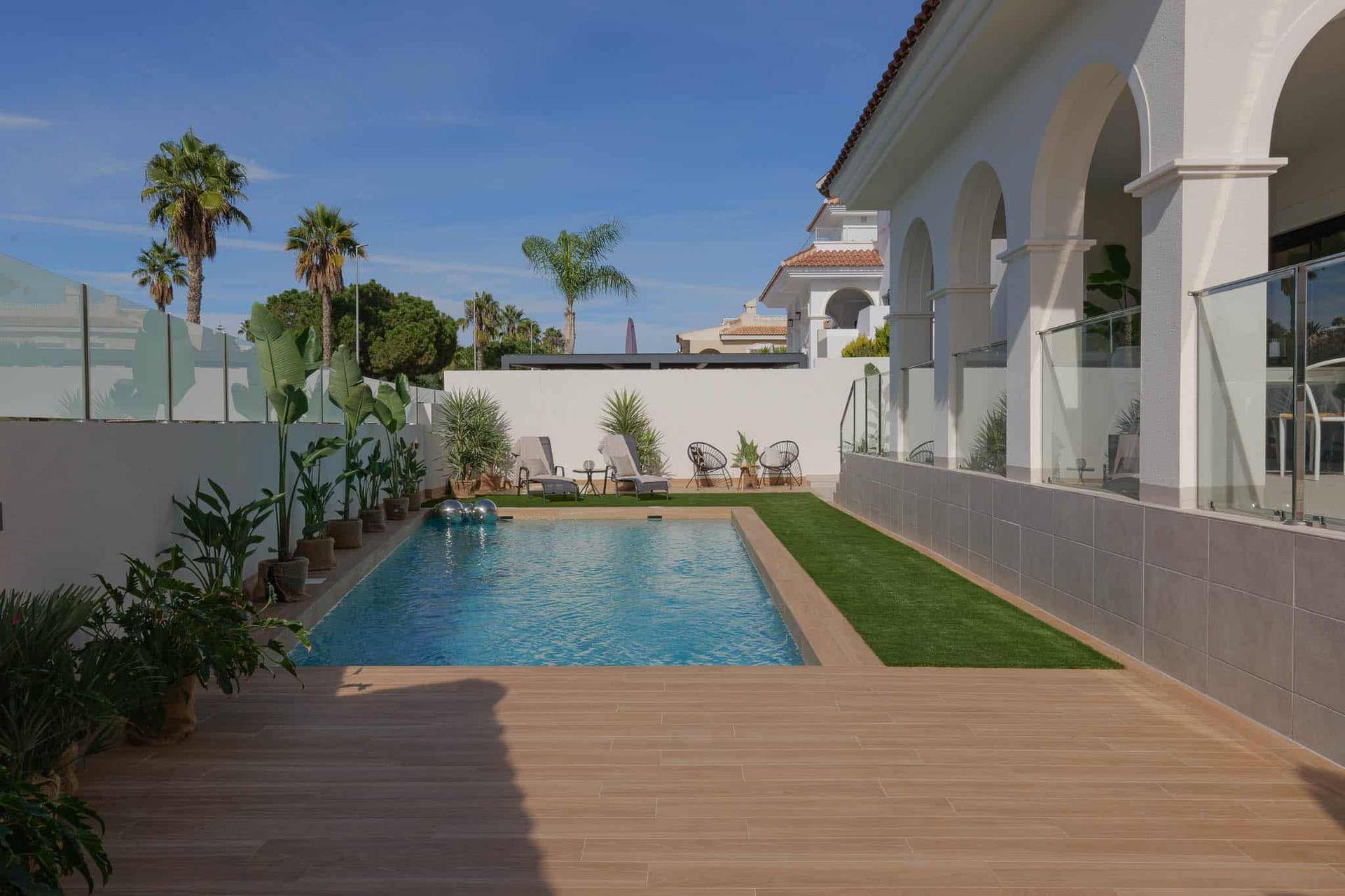 Moderner Poolbereich mit Holzdeck, Kunstrasen und bequemen Liegestühlen in sonniger Umgebung.