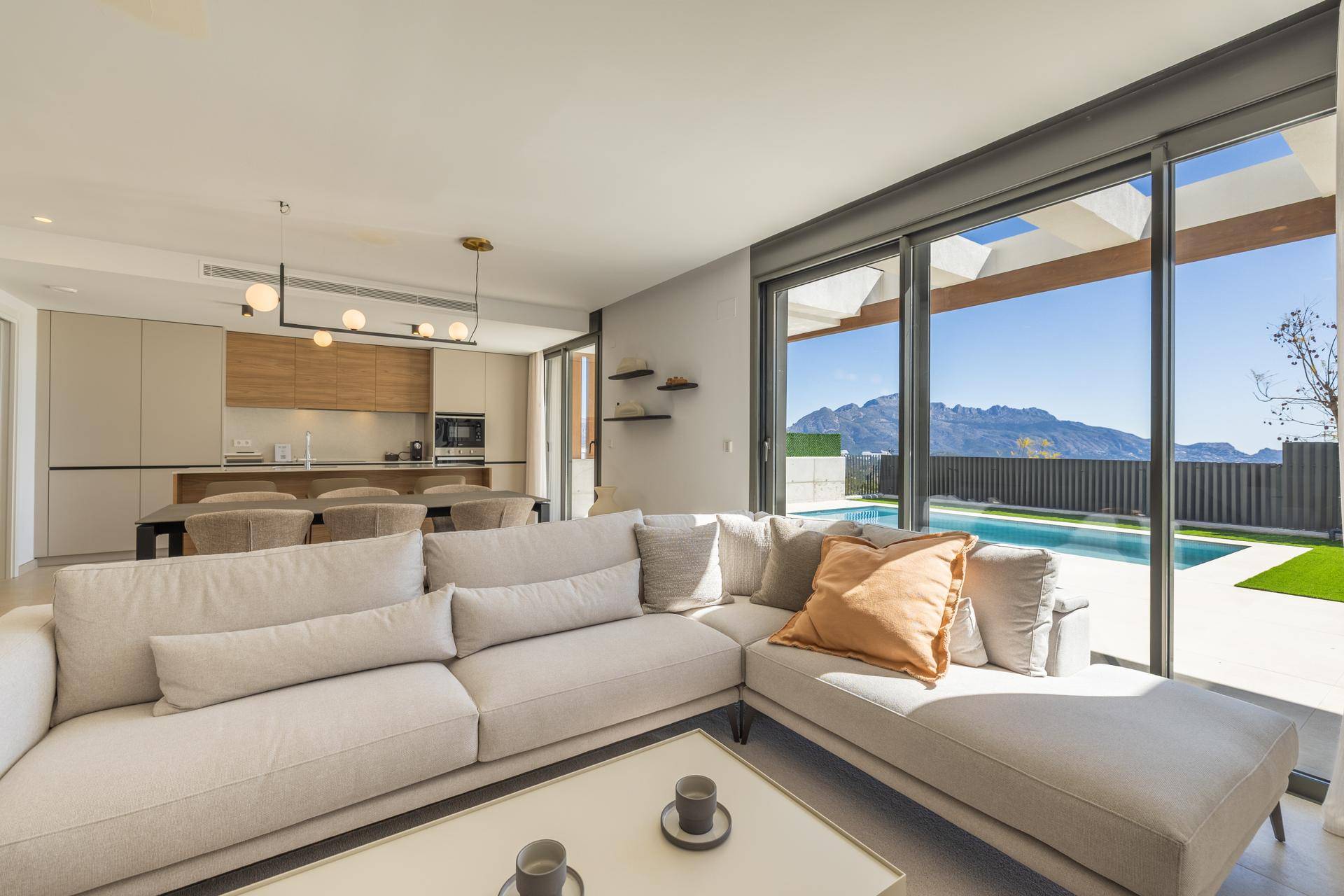 Helles Wohnzimmer mit bequemer Couch, großen Fenstern und Panoramablick auf Pool und Berge.