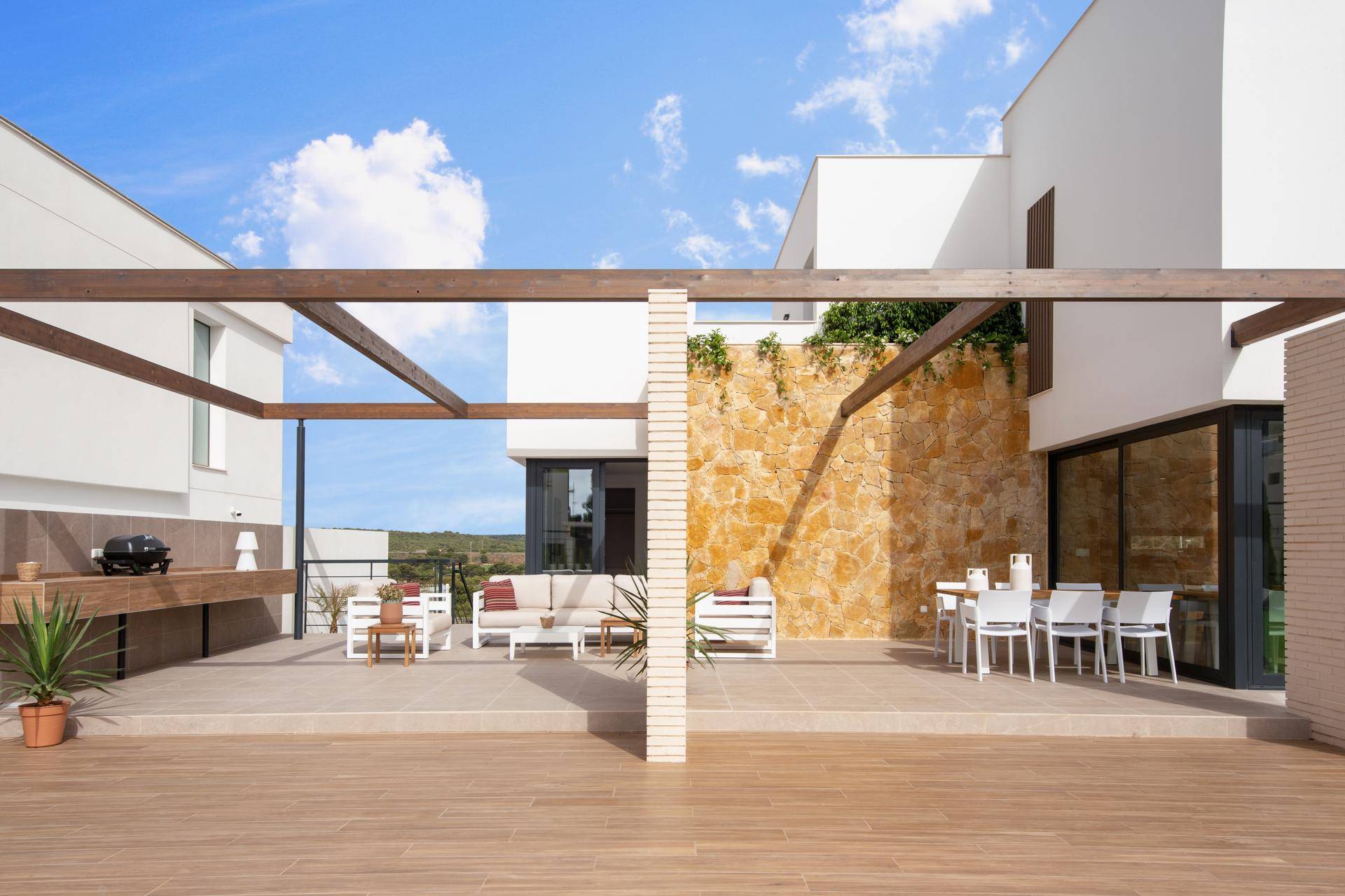 Geräumige Terrasse mit Essbereich, Lounge-Möbeln und integrierter Außenküche, umgeben von Naturstein.