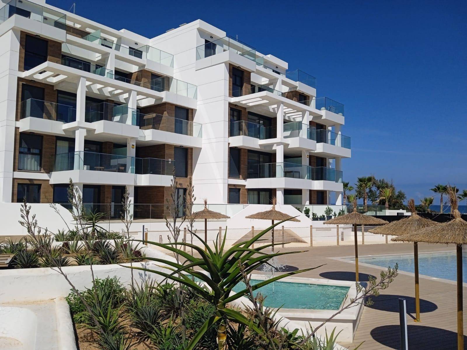 Ansicht des modernen Apartmentgebäudes mit Poolbereich, Strohschirmen und tropischen Pflanzen.