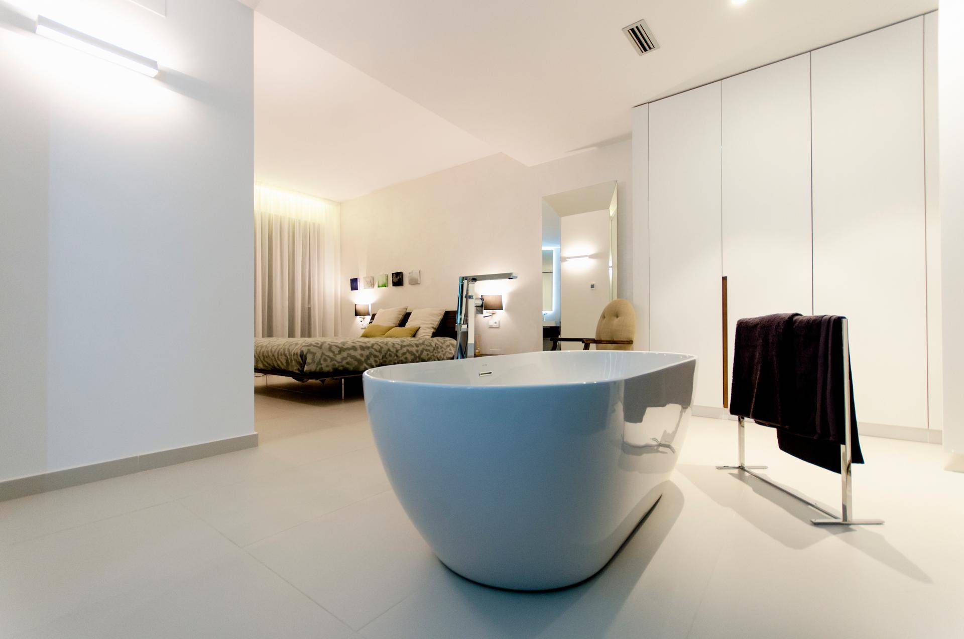 Helles Schlafzimmer mit freistehender Badewanne und Blick auf den Schlafbereich.