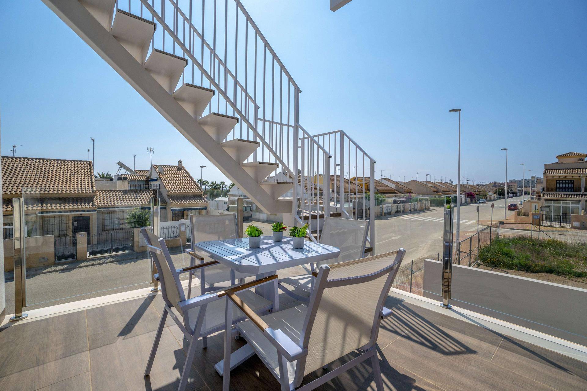 Sonniger Balkon mit Glasgeländer und Blick auf die umliegende Wohnsiedlung und Straße.