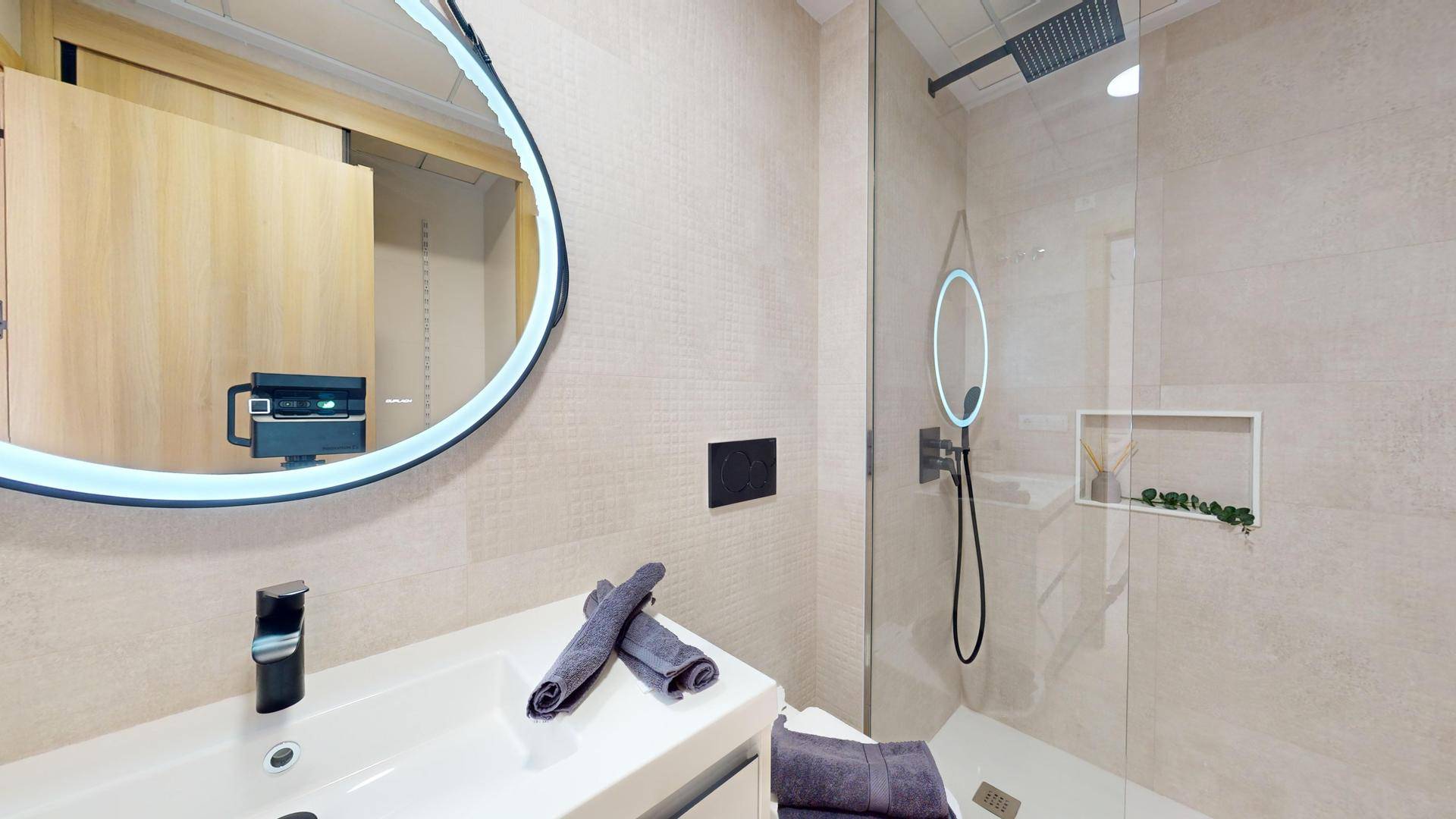Modernes Badezimmer mit begehbarer Dusche, stilvollem Waschbecken und beleuchtetem Spiegel.
