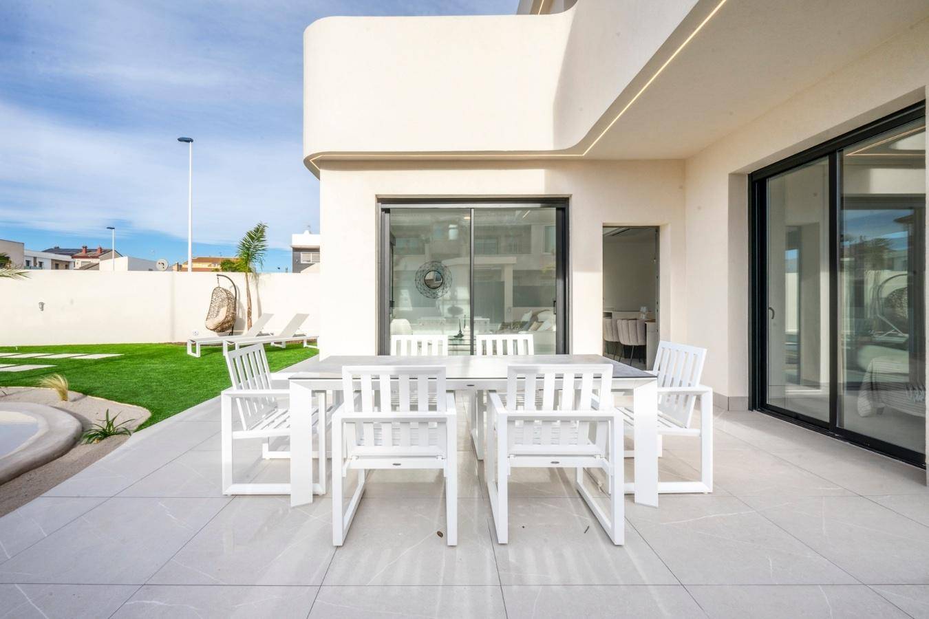 Helle Terrasse mit modernem Esstisch und Stühlen, direktem Zugang zum Haus und Blick auf den Garten.