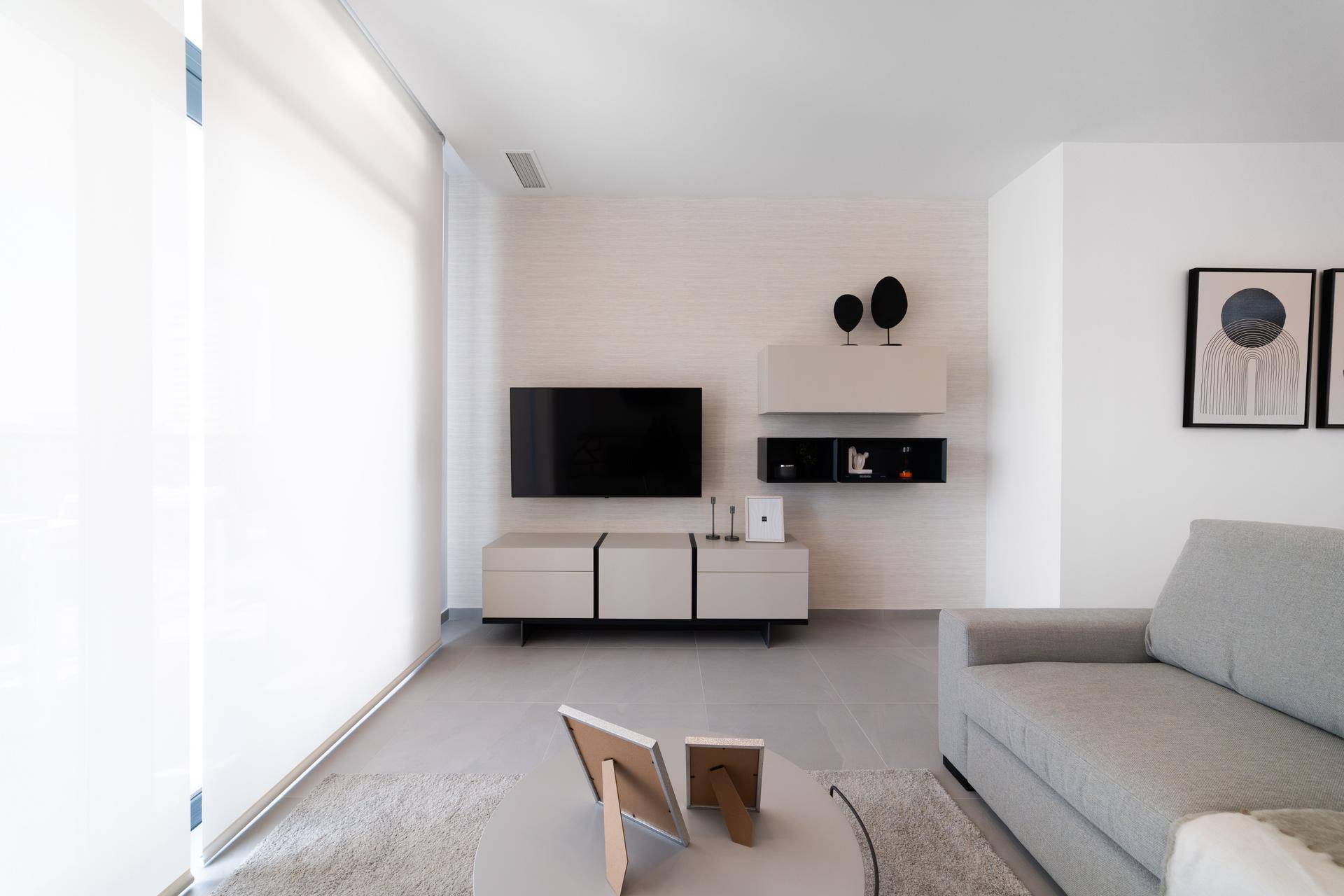 Modernes Wohnzimmer mit Flachbildfernseher, minimalistischen Möbeln und großen Fenstern.
