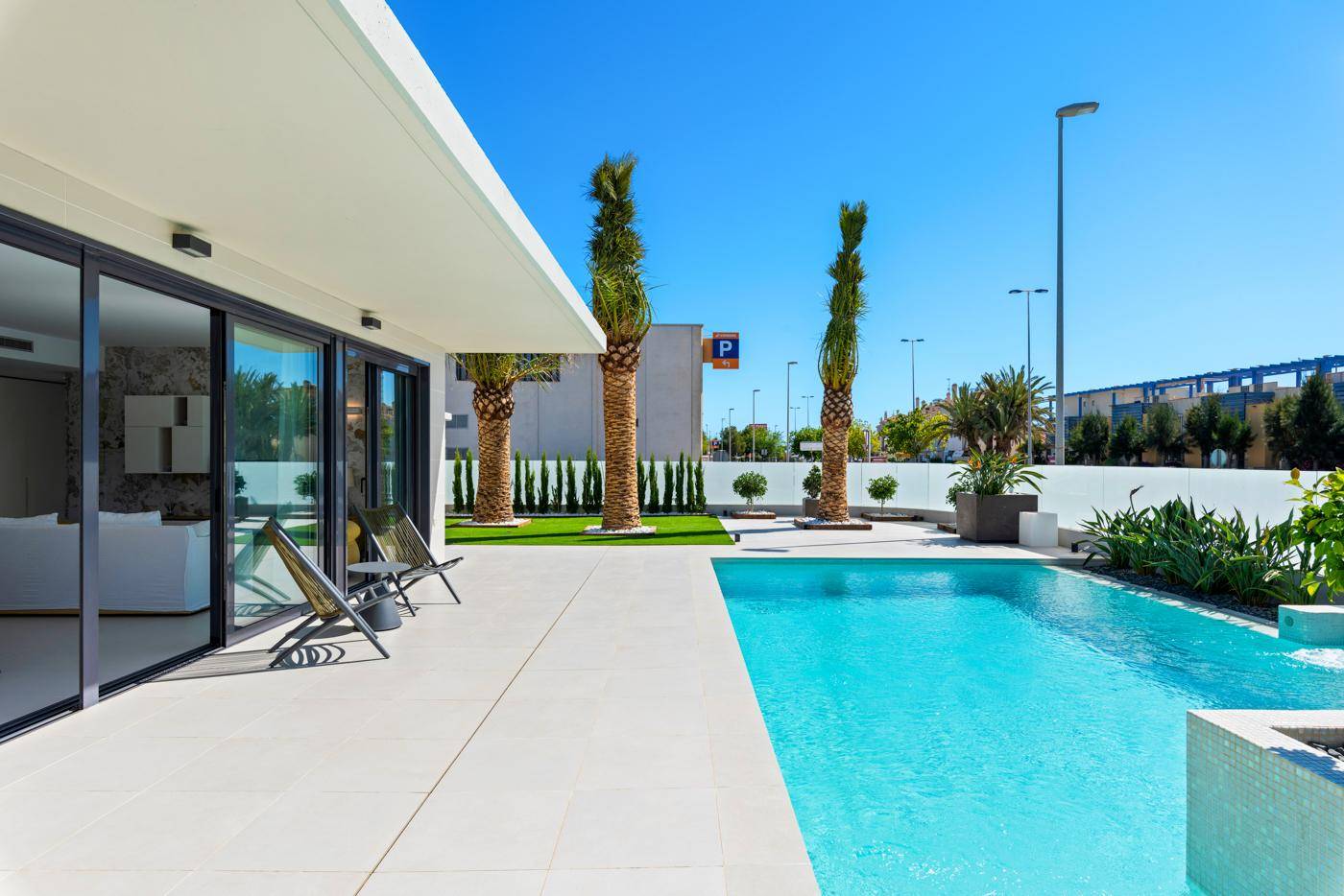 Geräumiger Poolbereich mit Liegestühlen, Palmen und direktem Zugang zum Haus unter blauem Himmel.
