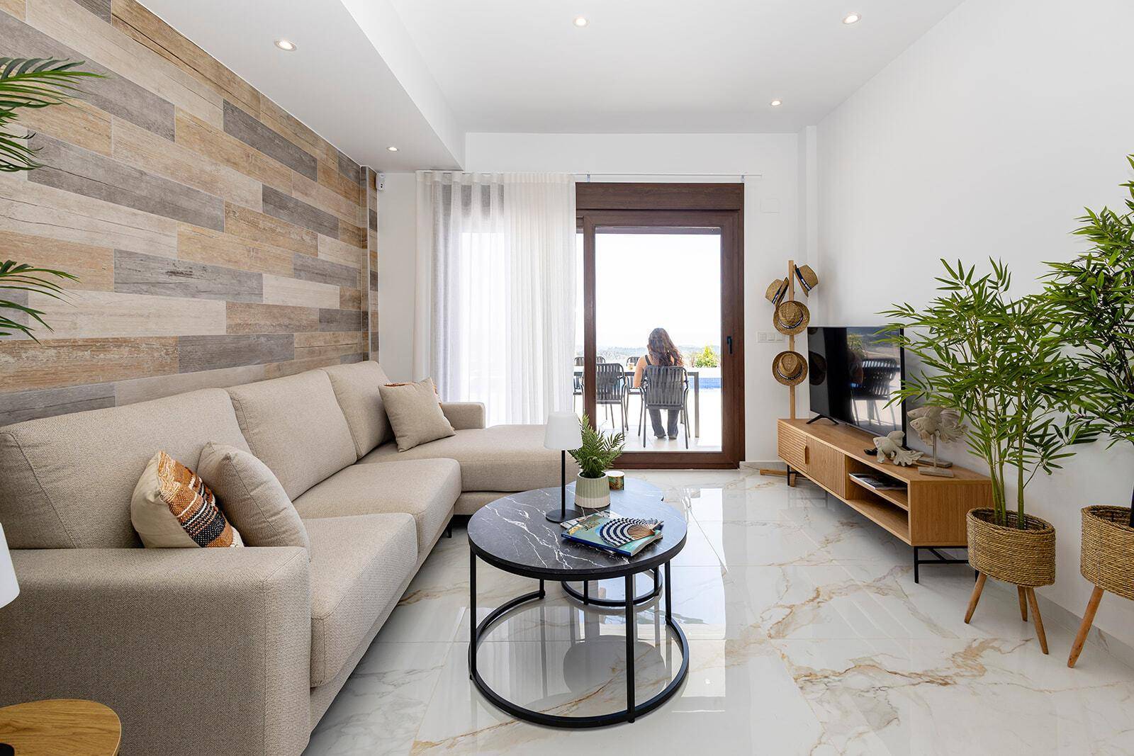 Gemütliches Wohnzimmer mit beiger Couch, Holzwand und Zugang zur sonnigen Terrasse.
