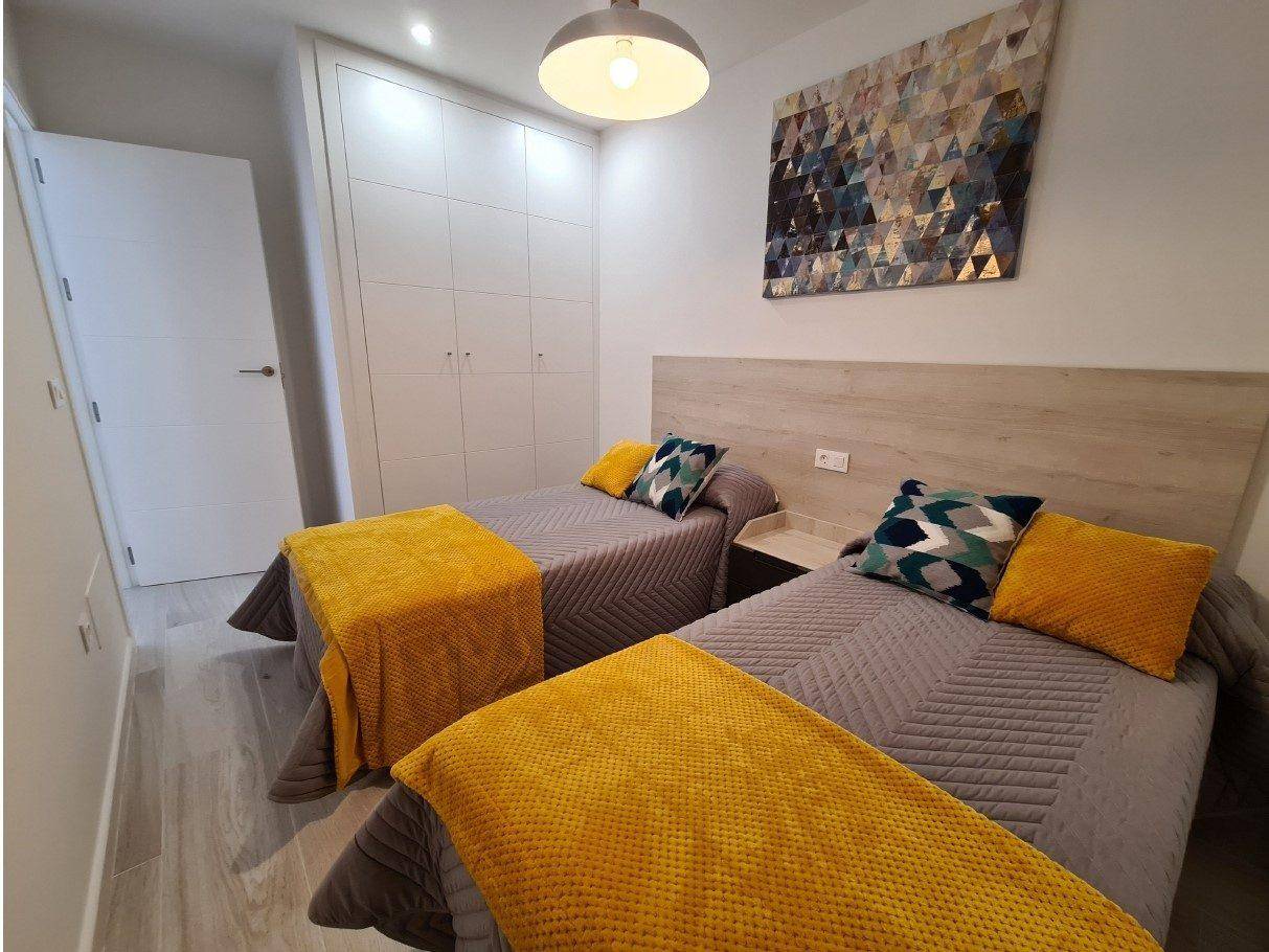 Helles Schlafzimmer mit zwei Einzelbetten, Einbauschränken und farbigen Akzenten.