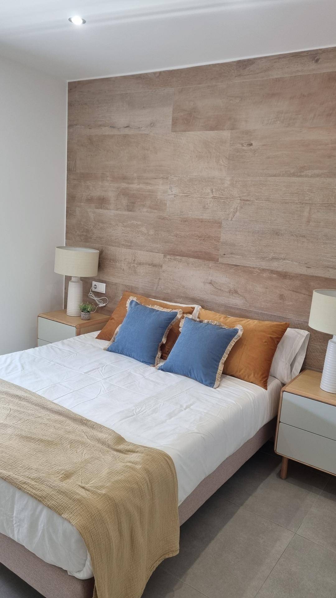Schlafzimmer mit Holzwandverkleidung hinter dem Bett und modernen Nachttischen.