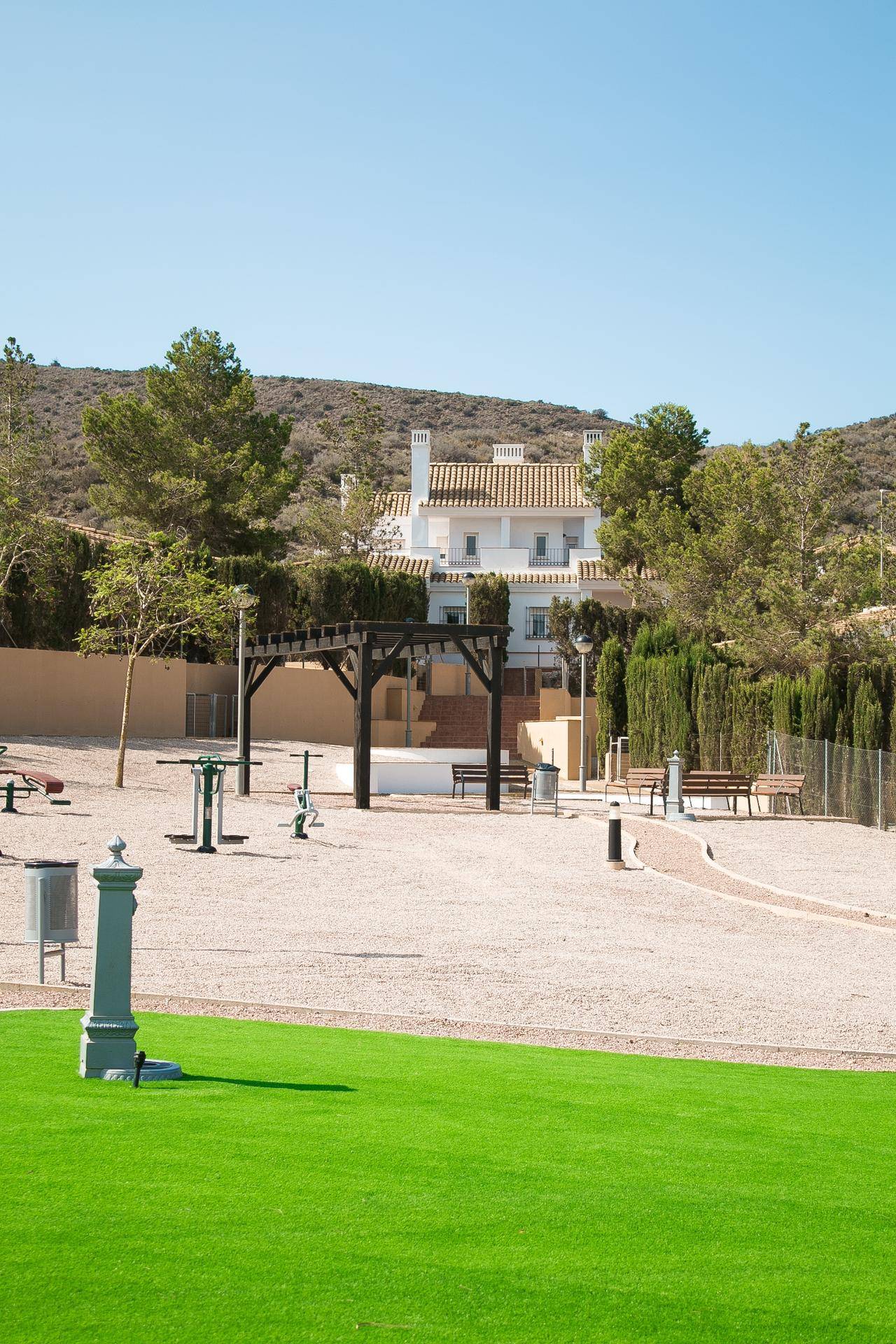 Öffentlicher Park mit Fitnessgeräten und einem Wohnhaus im Hintergrund, umgeben von Hügeln.