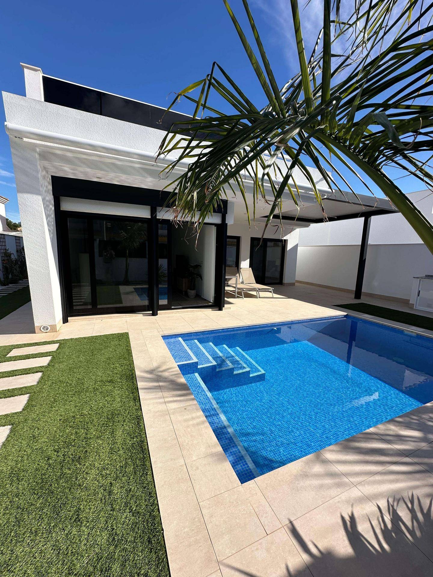 Blick auf den privaten Poolbereich mit Liegestuhl und moderner Architektur unter blauem Himmel.