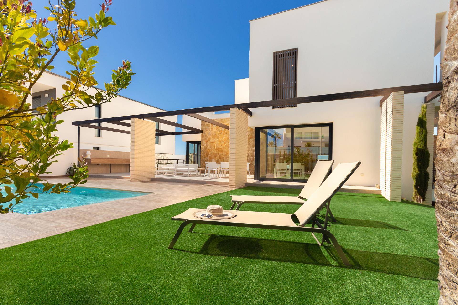 Sonnige Rasenfläche mit bequemen Liegestühlen neben dem Pool und der modernen Architektur des Hauses.