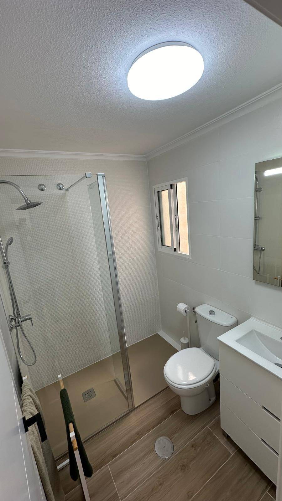 Helles Badezimmer mit moderner Duschkabine, WC und Fenster.