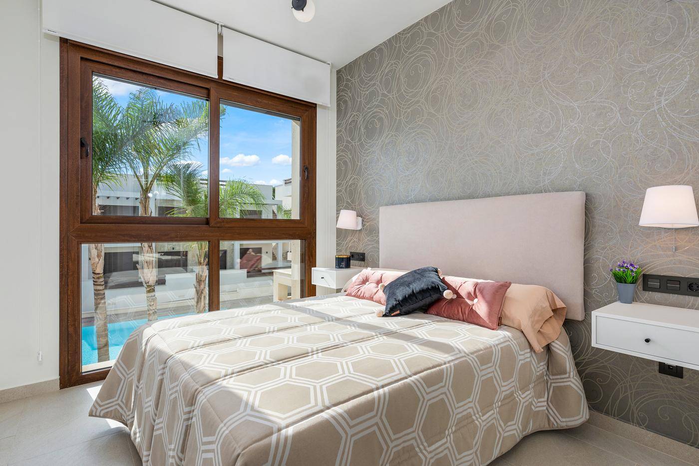 Schlafzimmer mit Doppelbett und großen Fenstern, die einen direkten Blick auf den Pool und Palmen bieten.