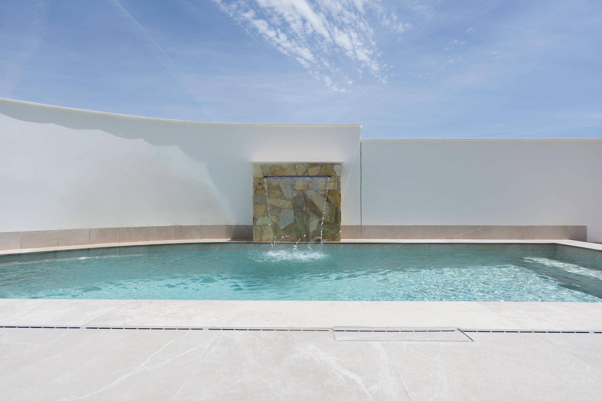 Privater Pool mit elegantem Wasserfall und hellen Fliesen im Außenbereich.