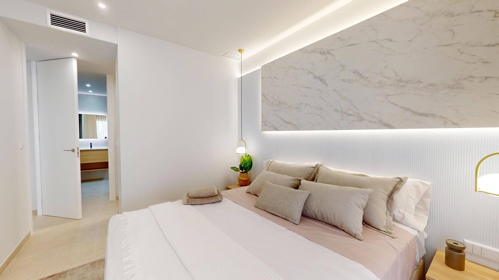 Helles Schlafzimmer mit modernem Kopfteil und direktem Zugang zu einem eleganten Badezimmer.