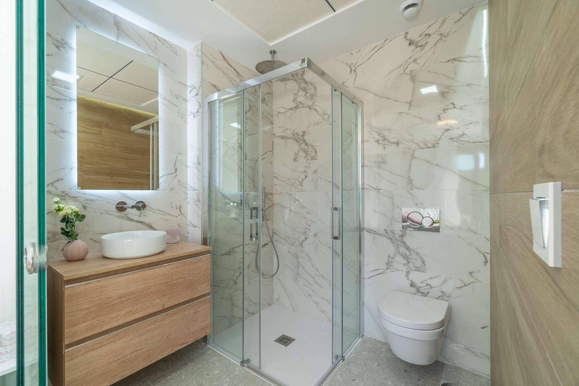 Elegantes Badezimmer mit moderner Duschkabine, wandhängendem WC und Waschtisch mit Holzunterschrank.