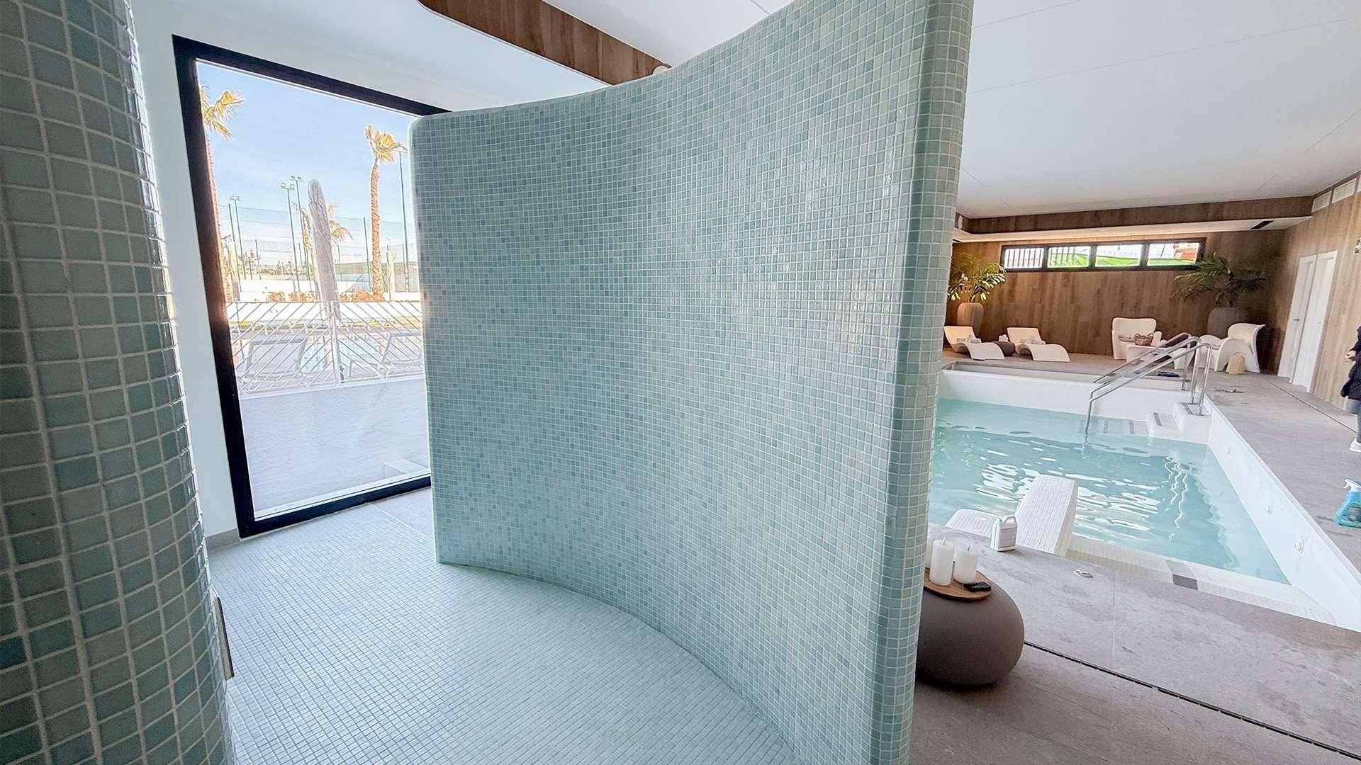 Duschbereich mit blauen Mosaikfliesen und Blick auf den Innenpool im Wellnessbereich.