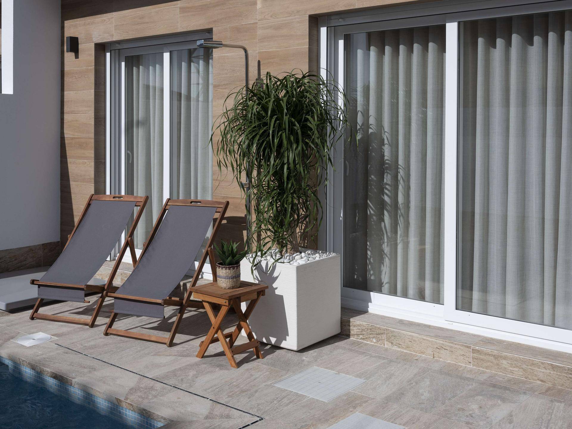 Sonniger Patio mit kleinem Pool, Liegestühlen und großen Schiebetüren zum Haus.