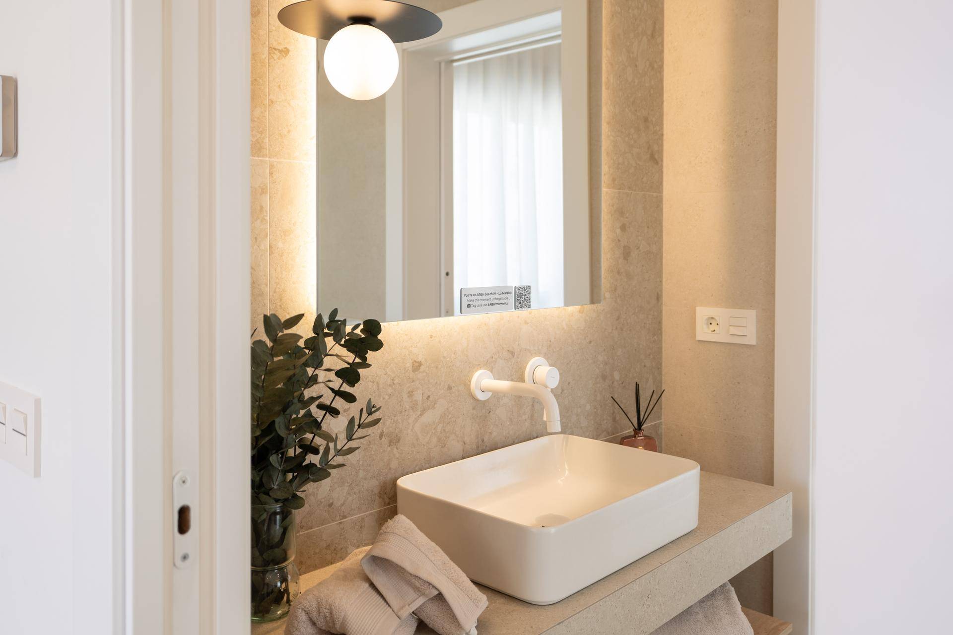 Detailansicht des Einzelwaschbeckens mit beleuchtetem Spiegel und moderner Armatur.