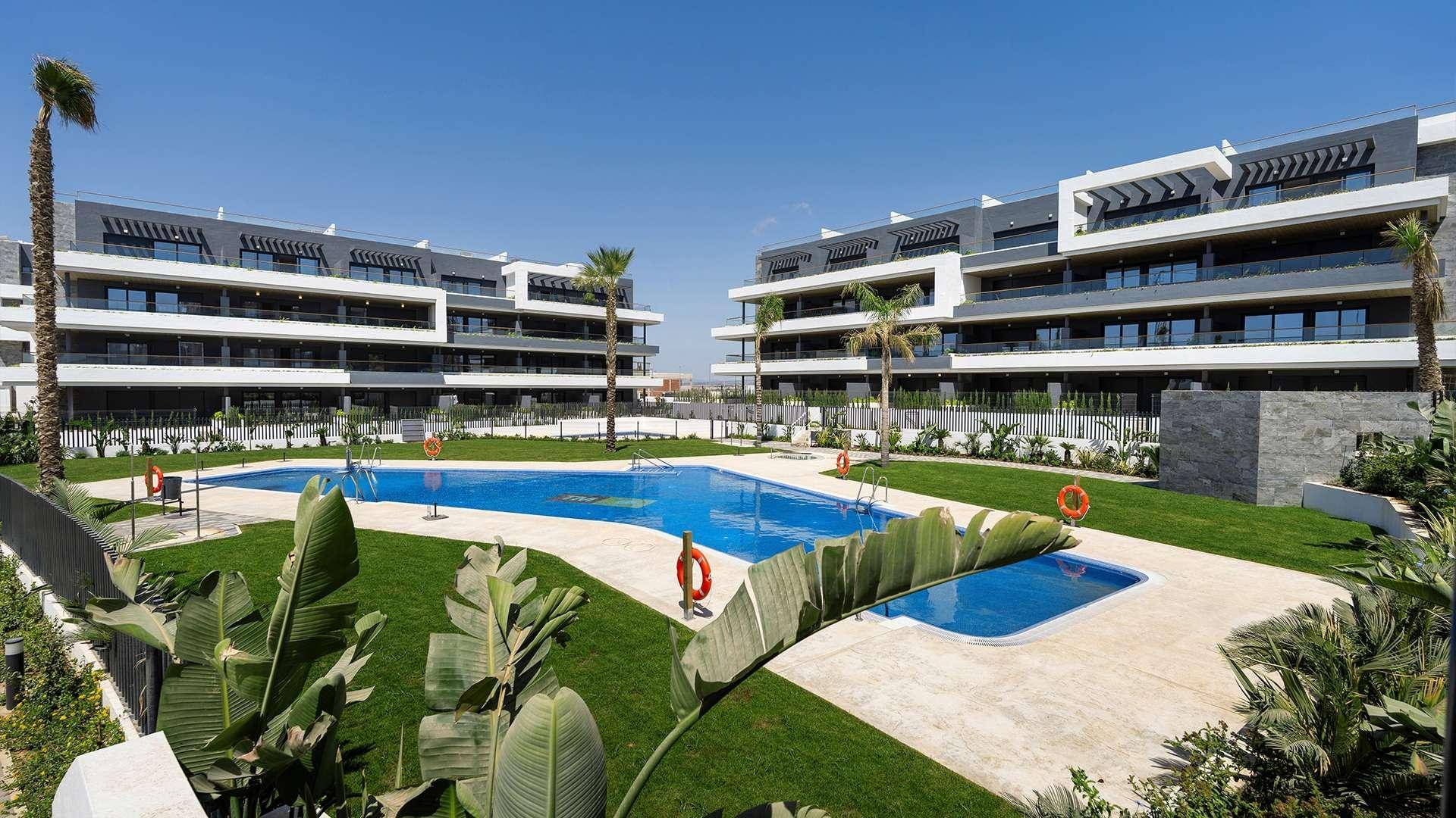 Weitläufige Apartmentanlage mit großem Poolbereich, gepflegtem Rasen und tropischen Pflanzen.