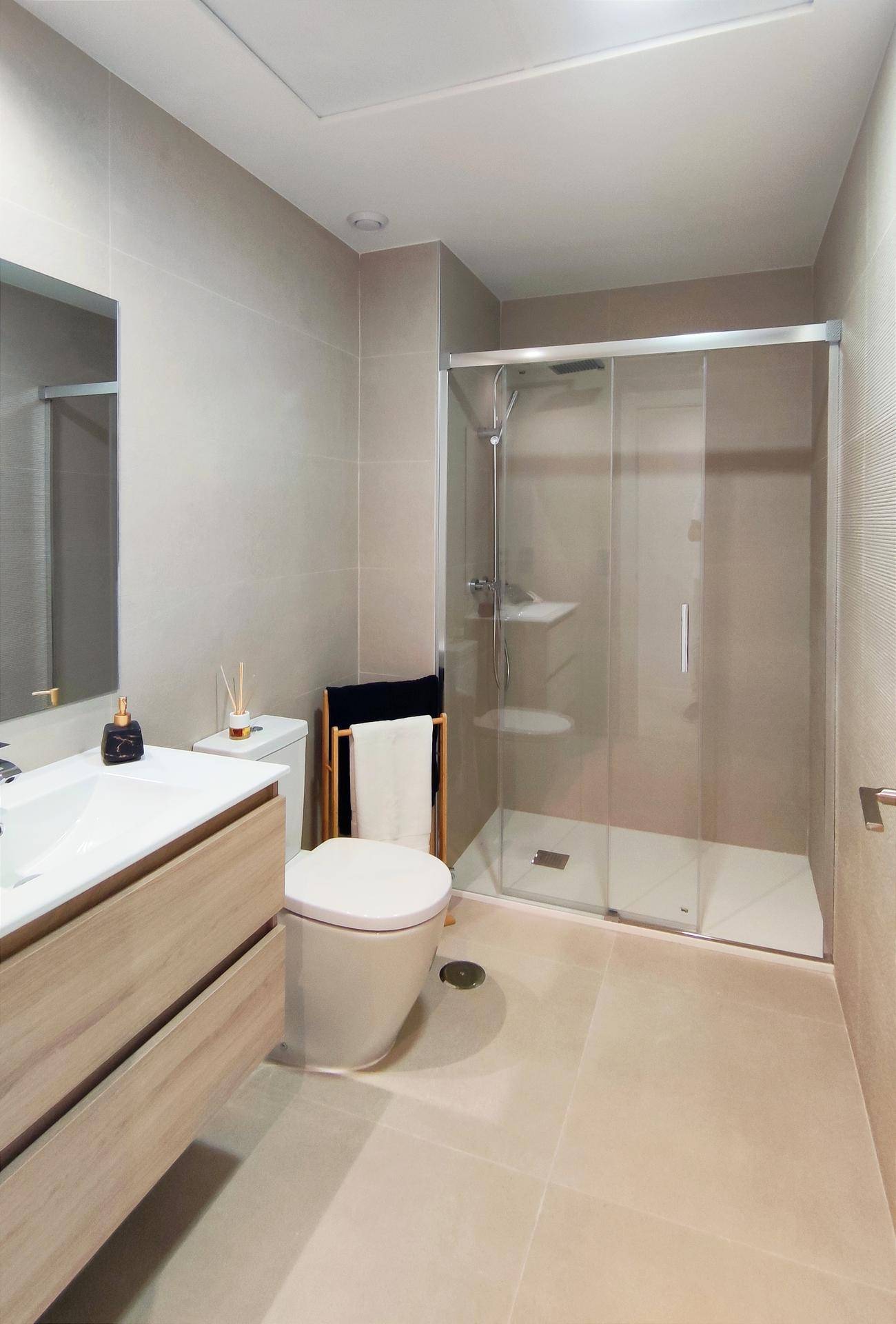 Modernes Badezimmer mit beigefarbenen Fliesen, Holzwaschtisch und großer Duschkabine.