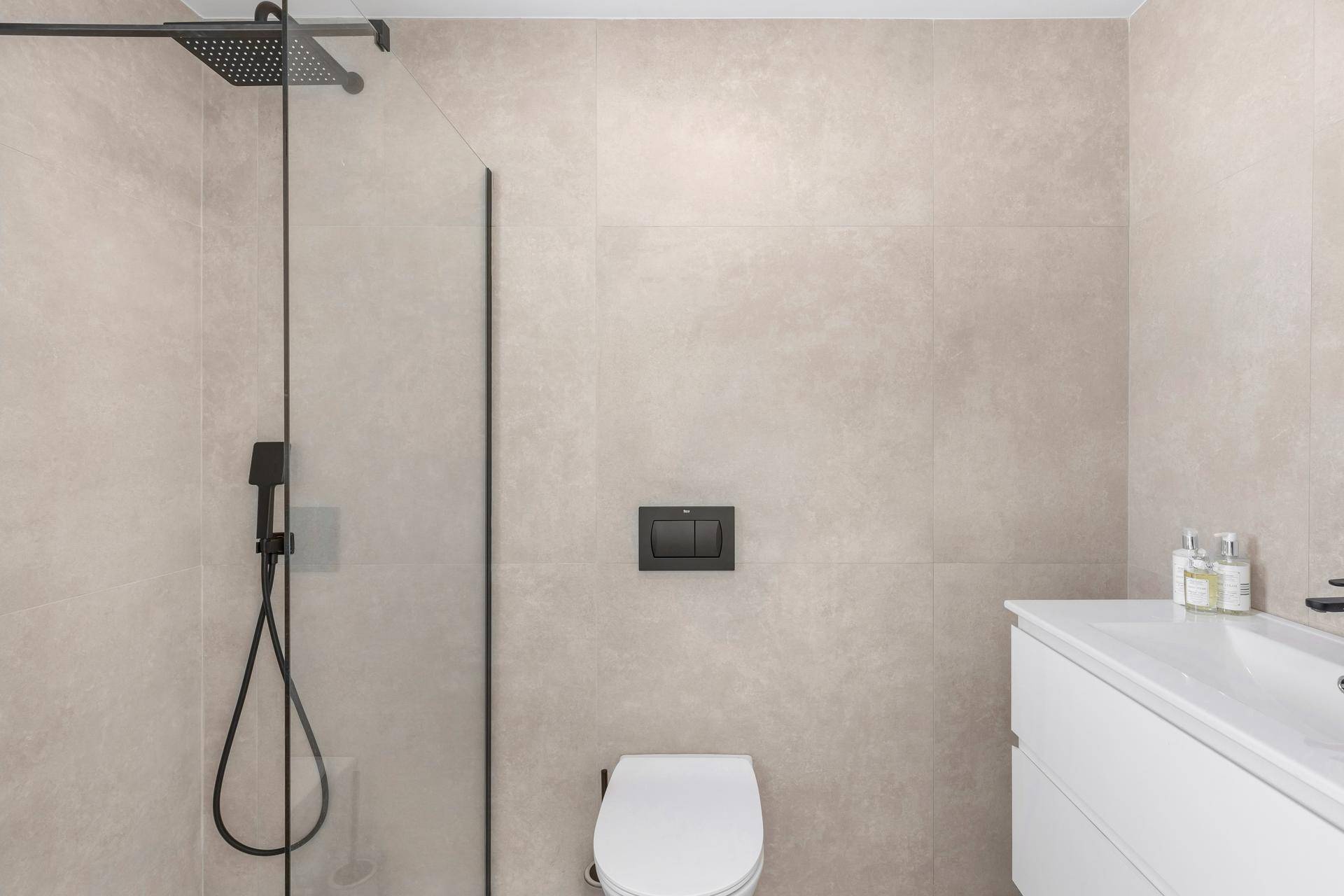 Modernes Badezimmer mit Dusche, WC und hellen, großformatigen Fliesen.