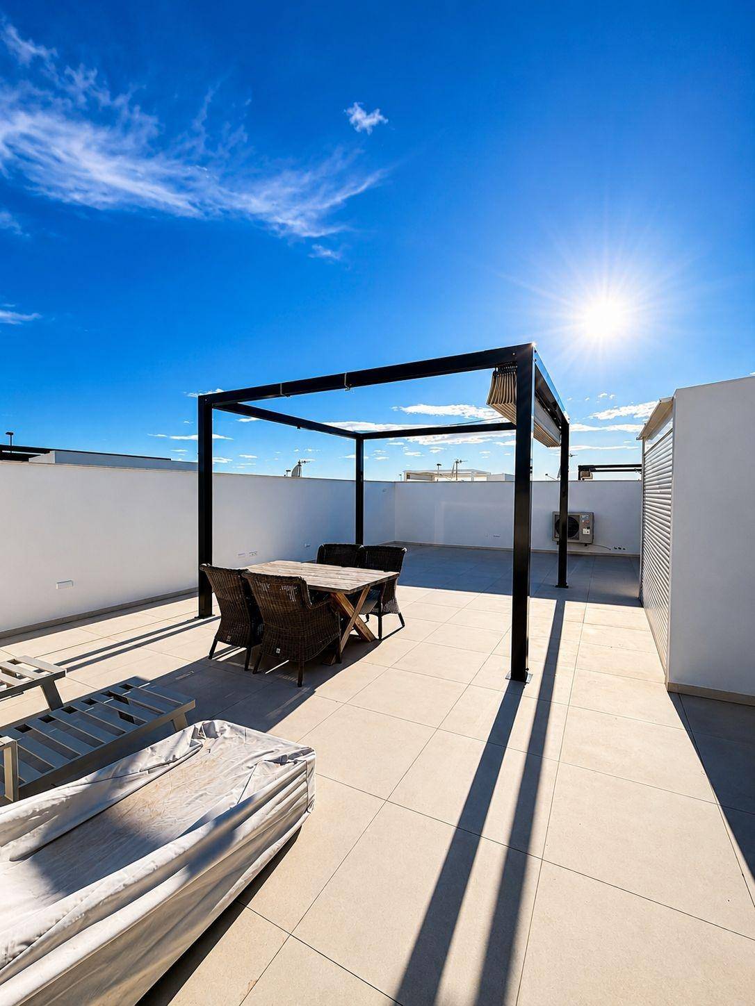 Sonniger Dachterrassenbereich mit Esstisch, Pergola und weitem Blick unter blauem Himmel.