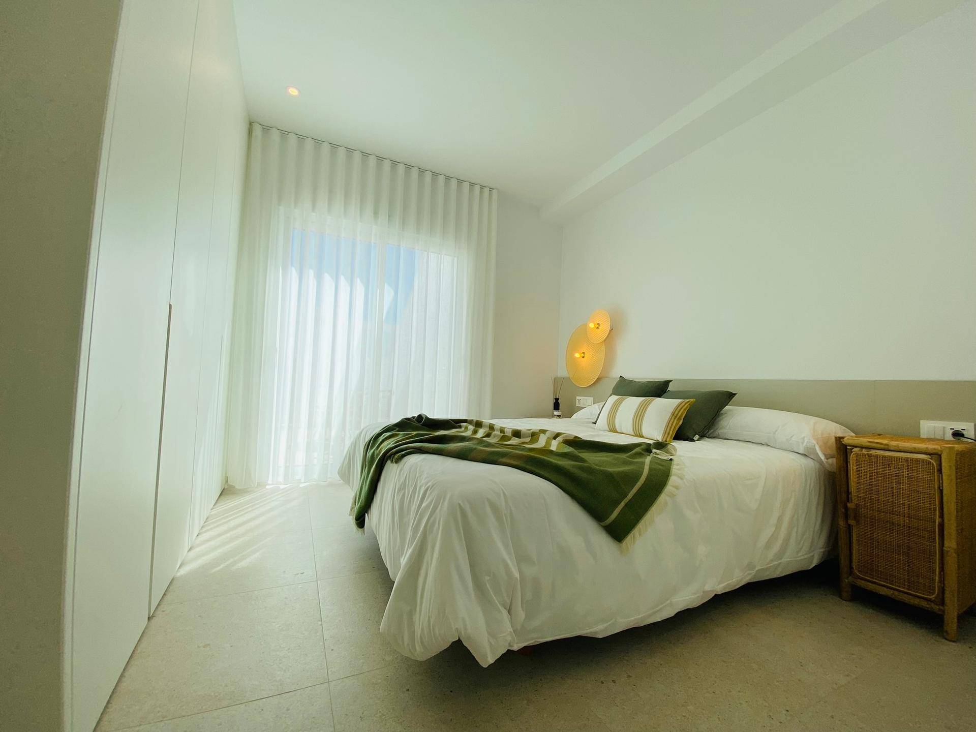 Helles Schlafzimmer mit großem Bett, Einbauschränken und viel Tageslicht durch das Fenster.