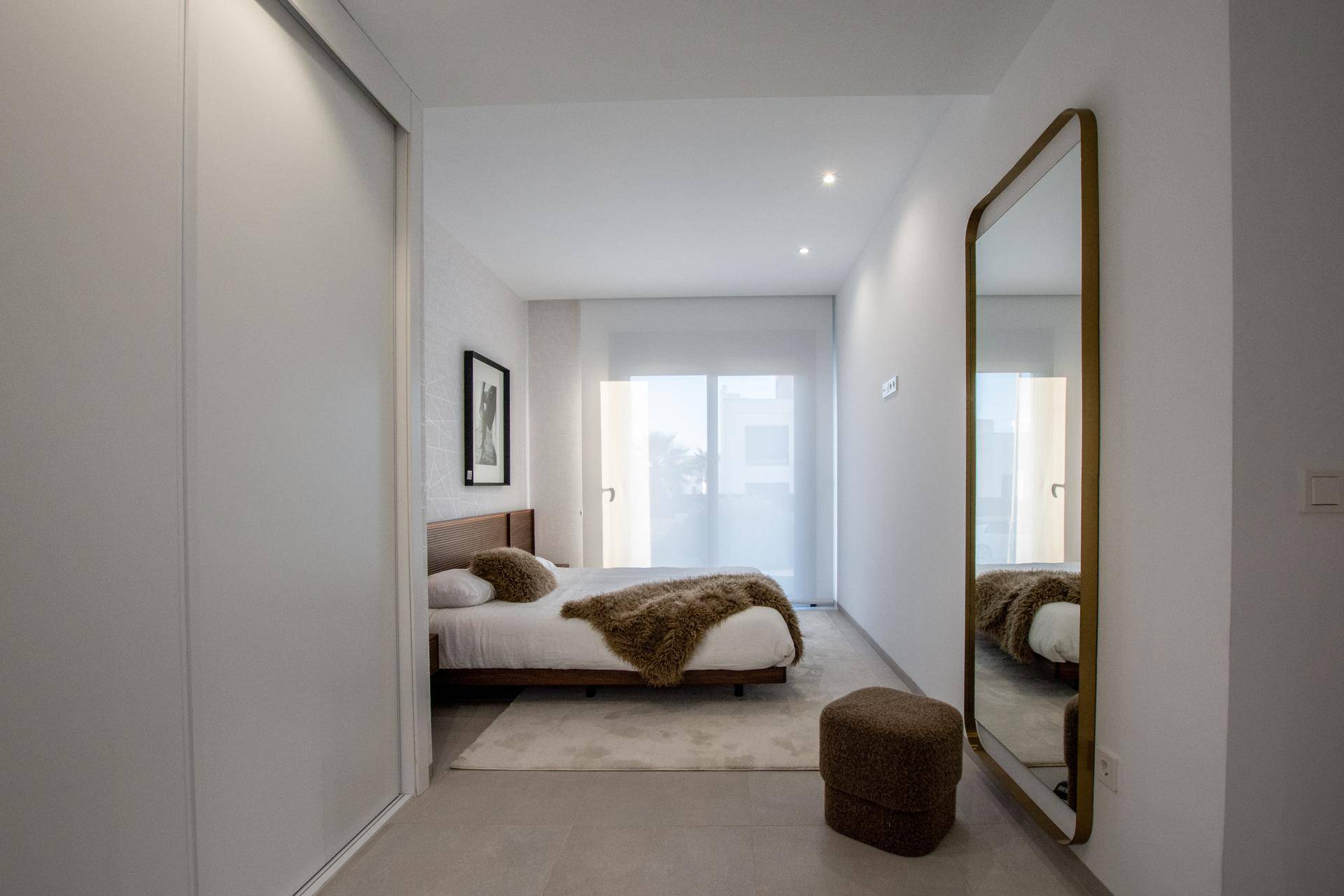 Helles Schlafzimmer mit modernem Bett, großem Spiegel und Schiebetüren zum Kleiderschrank.