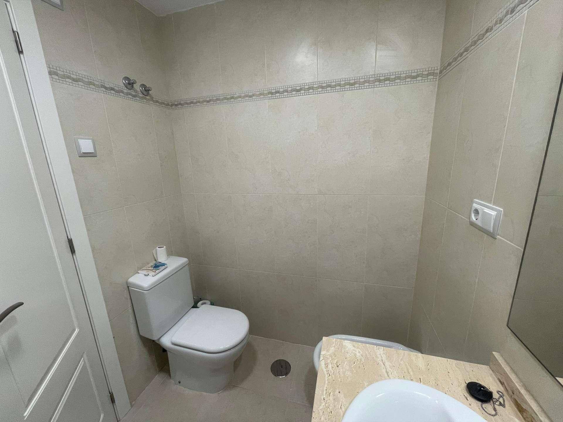 Separates WC mit Toilette, kleinem Waschbecken und Spiegel, komplett gefliest.