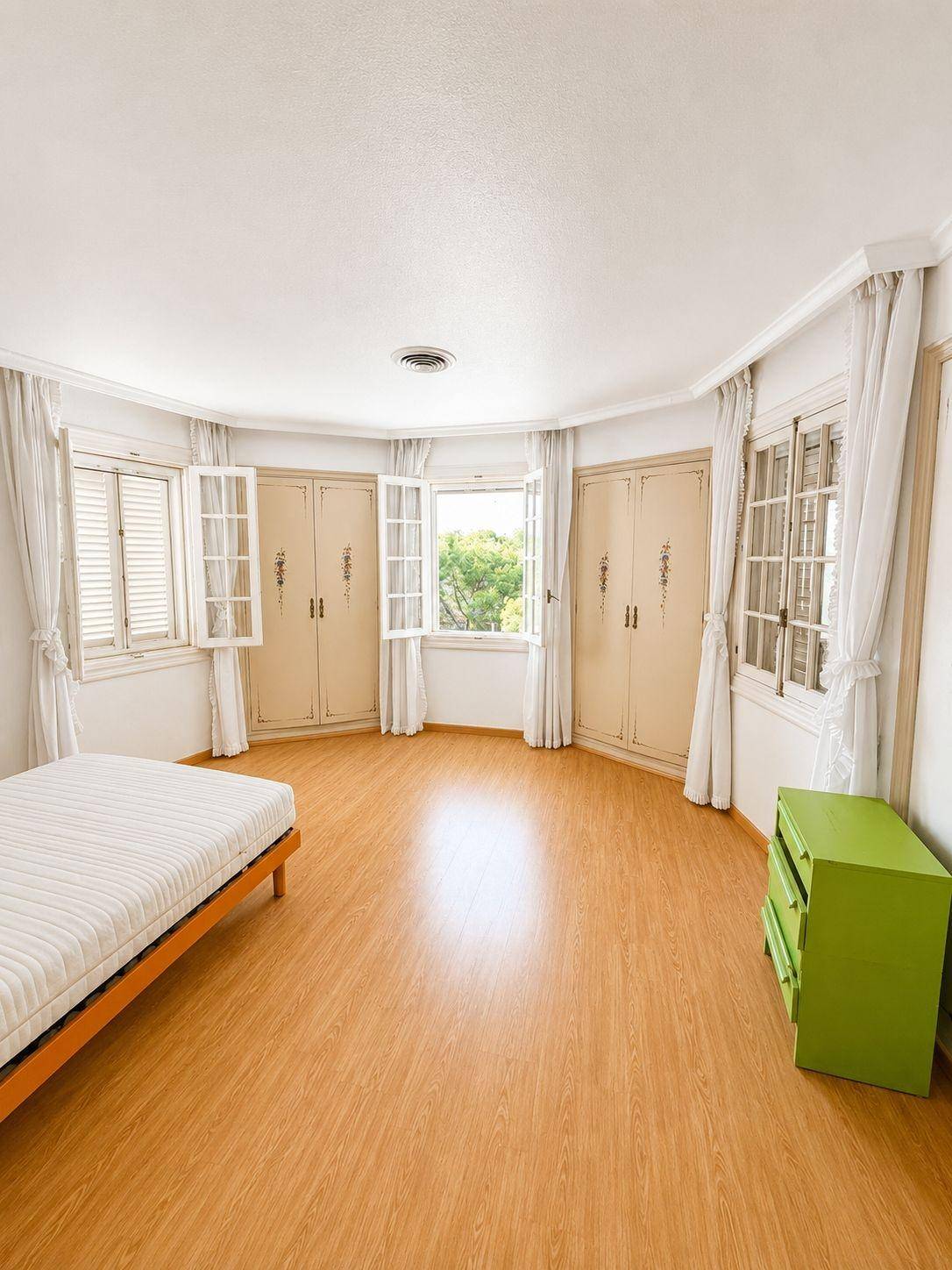 Helles Schlafzimmer mit Holzboden, Einbauschränken und mehreren Fenstern mit Blick ins Grüne.