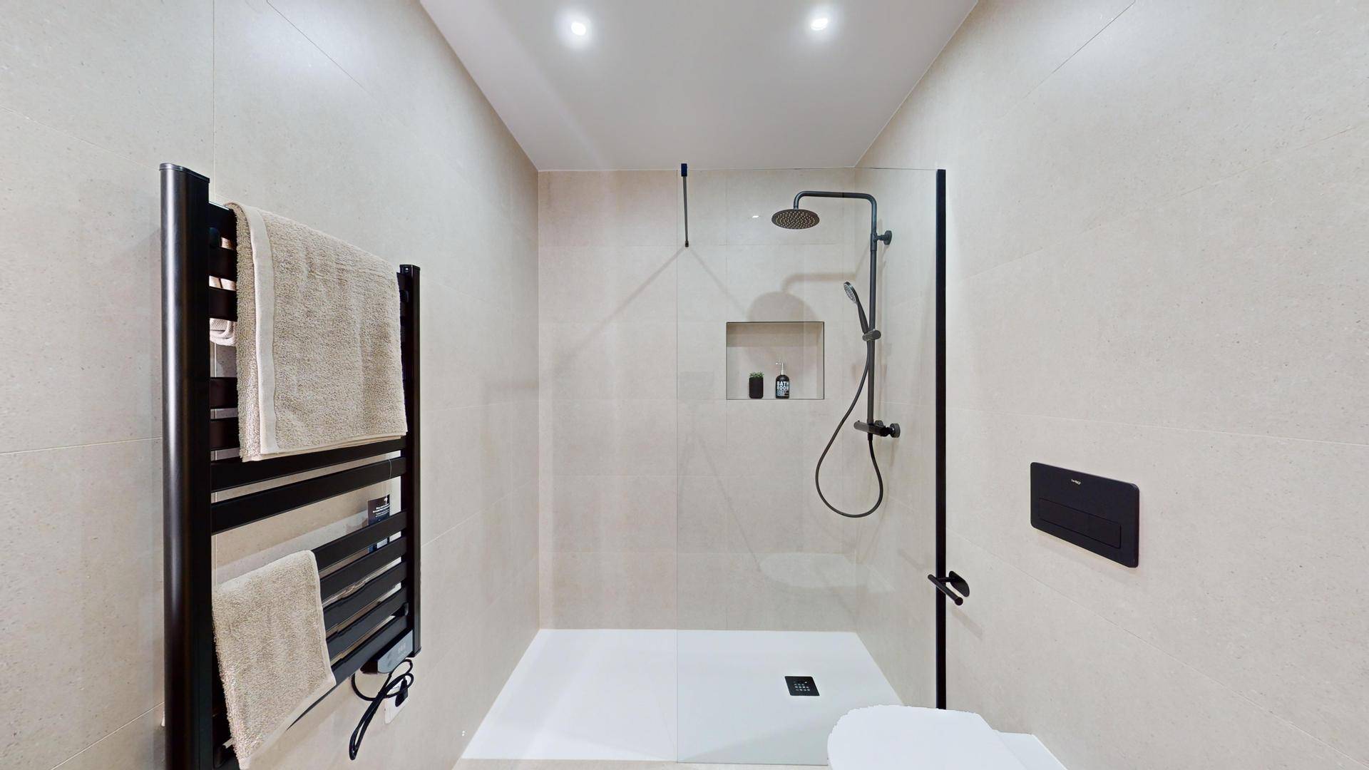 Geräumige begehbare Dusche mit Regenduschkopf, beheiztem Handtuchhalter und hellen Fliesen.