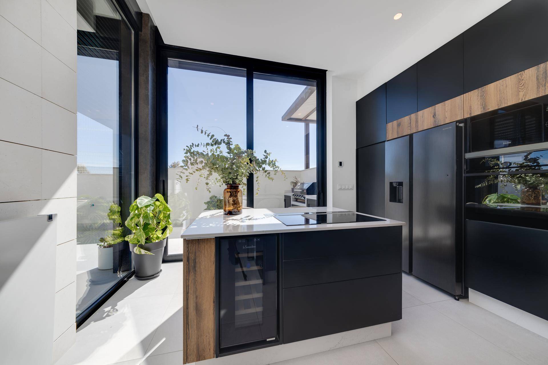 Moderne Küche mit dunklen Schränken, Holzdetails und heller Arbeitsplatte, mit Zugang zur Terrasse.