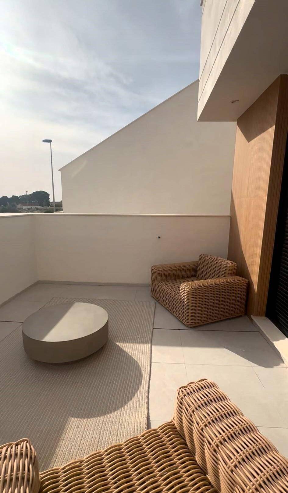 Sonnige Terrasse mit bequemen Rattan-Sesseln und einem runden Steintisch.