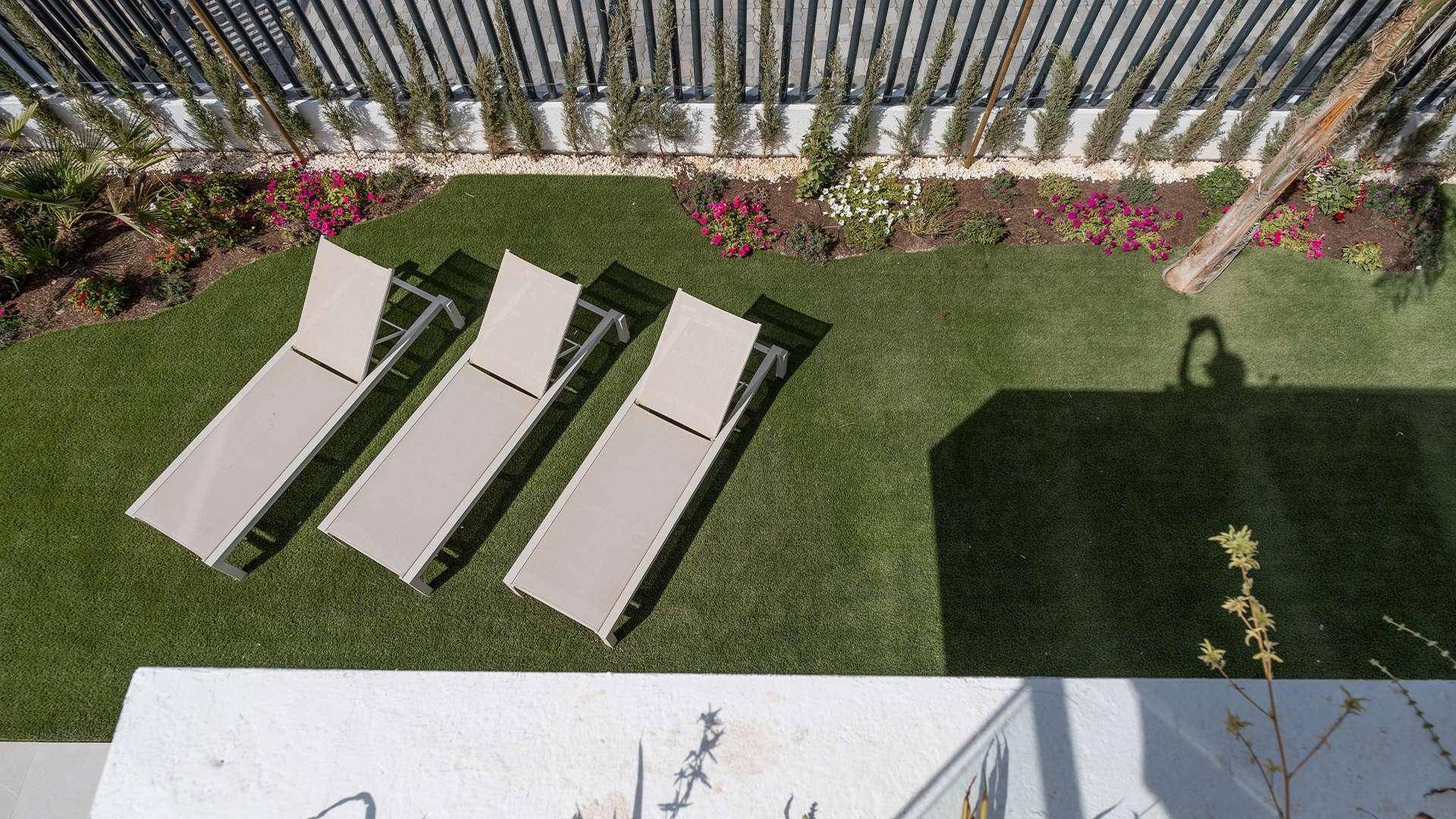 Vogelperspektive eines privaten Gartens mit Sonnenliegen auf Kunstrasen und Blumenbeeten.