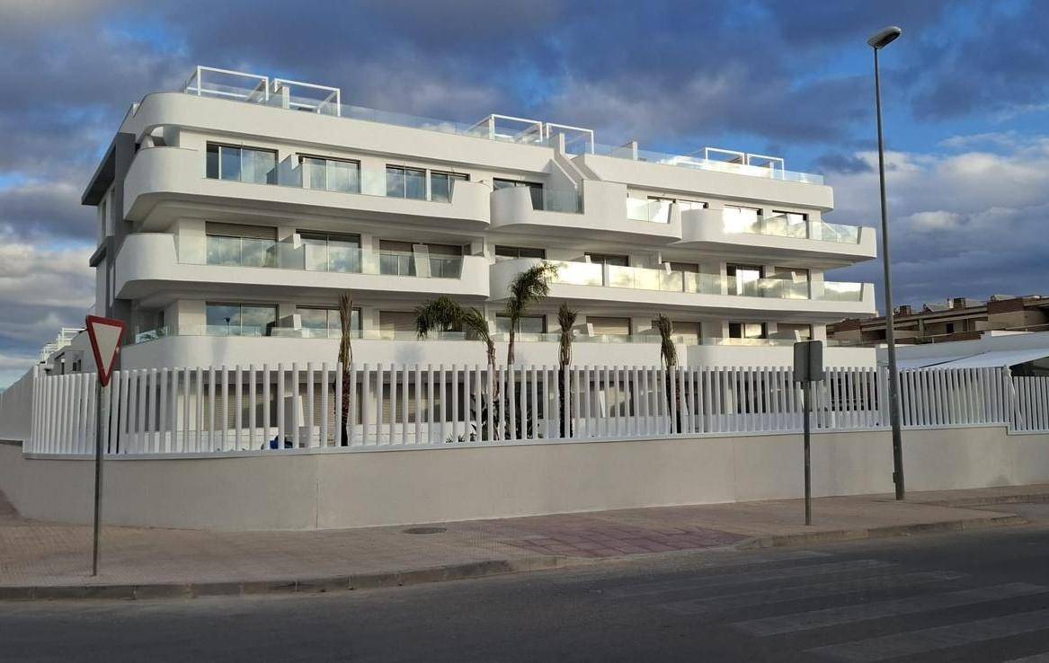 Elegante weiße Fassade eines modernen Apartmentgebäudes mit großen Glasbalkonen unter bewölktem Himmel.