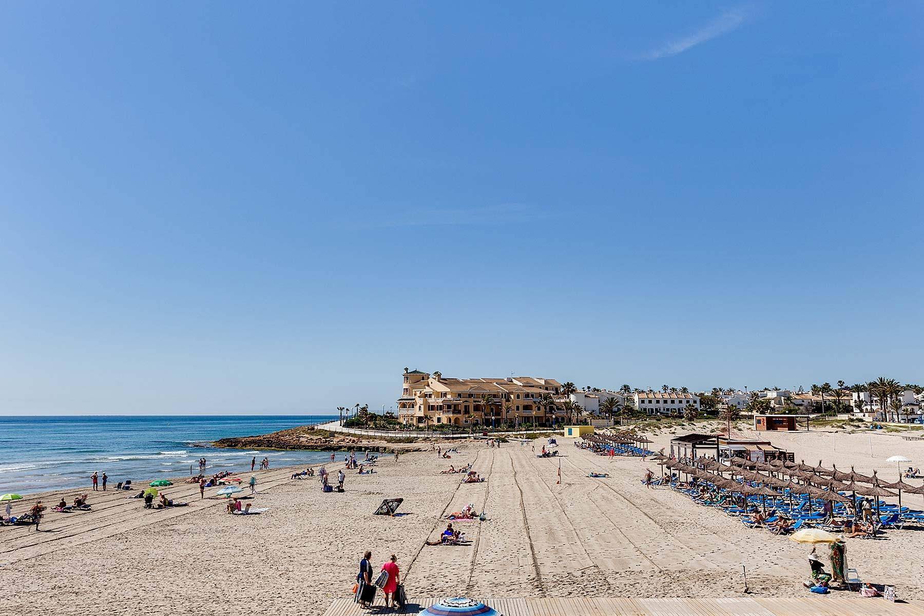 Weitläufiger Sandstrand mit vielen Badegästen, Sonnenschirmen und Gebäuden im Hintergrund.