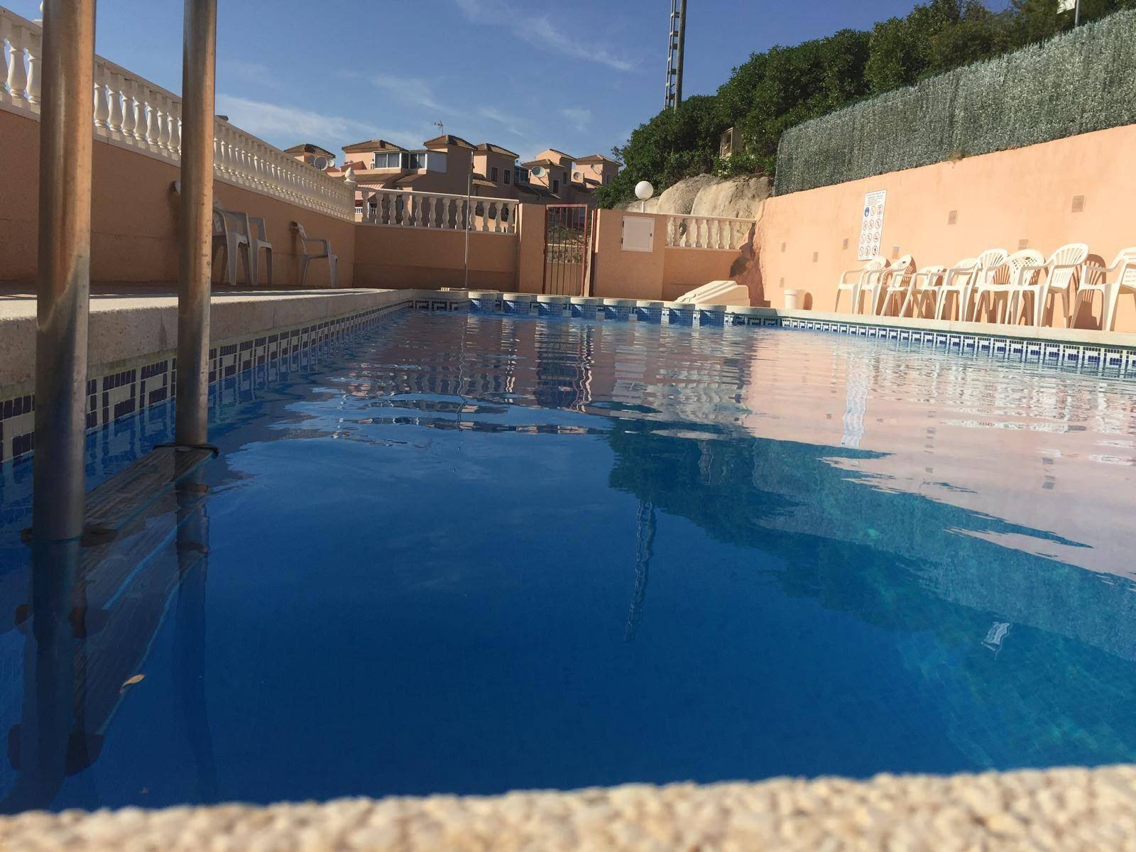 Langer Gemeinschaftspool mit blauen Fliesen und umliegender Terrasse an einem sonnigen Tag.