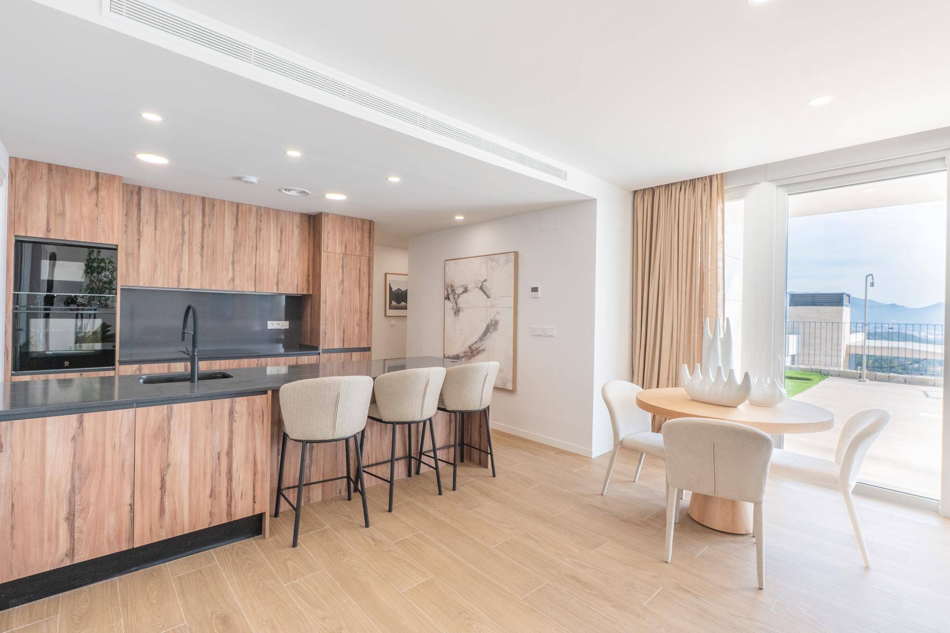 Moderne Küche mit Holzfronten, dunkler Arbeitsplatte und Essbereich mit Zugang zur Terrasse.