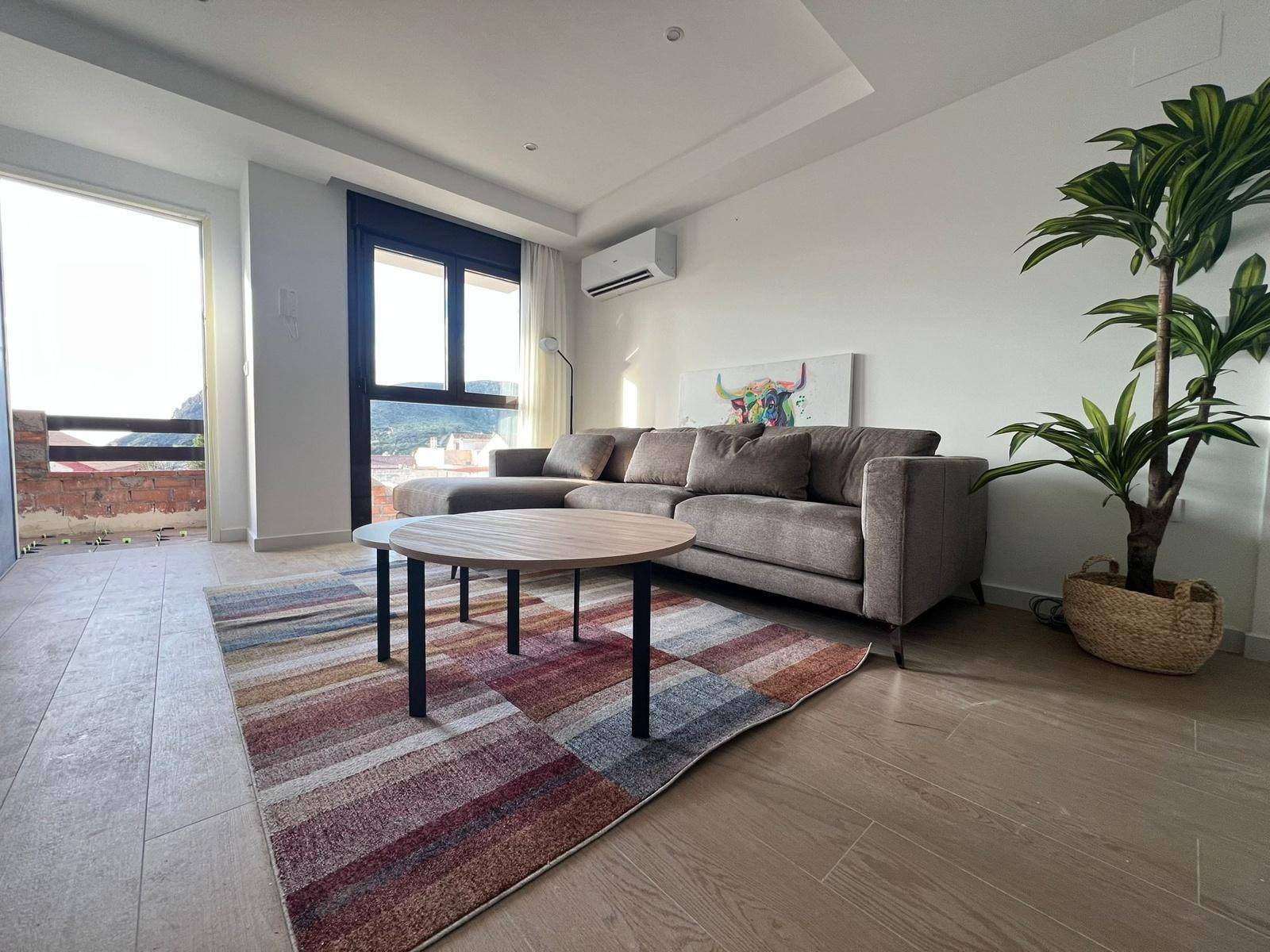 Modernes Wohnzimmer mit beigem Sofa, Holzboden und Zugang zu einem Balkon.