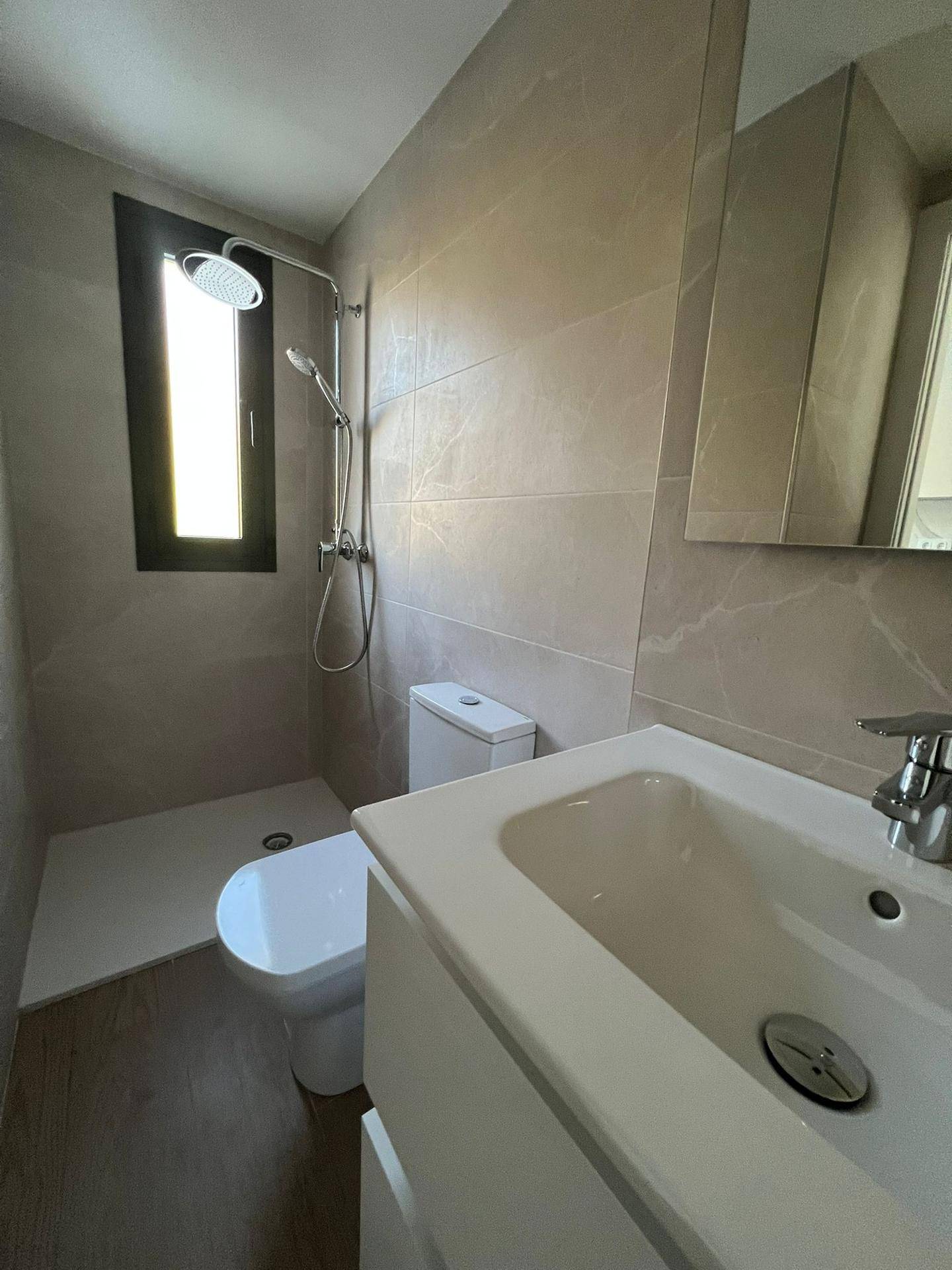 Modernes Badezimmer mit begehbarer Dusche, WC und Waschbecken, hell gefliest und mit Fenster.