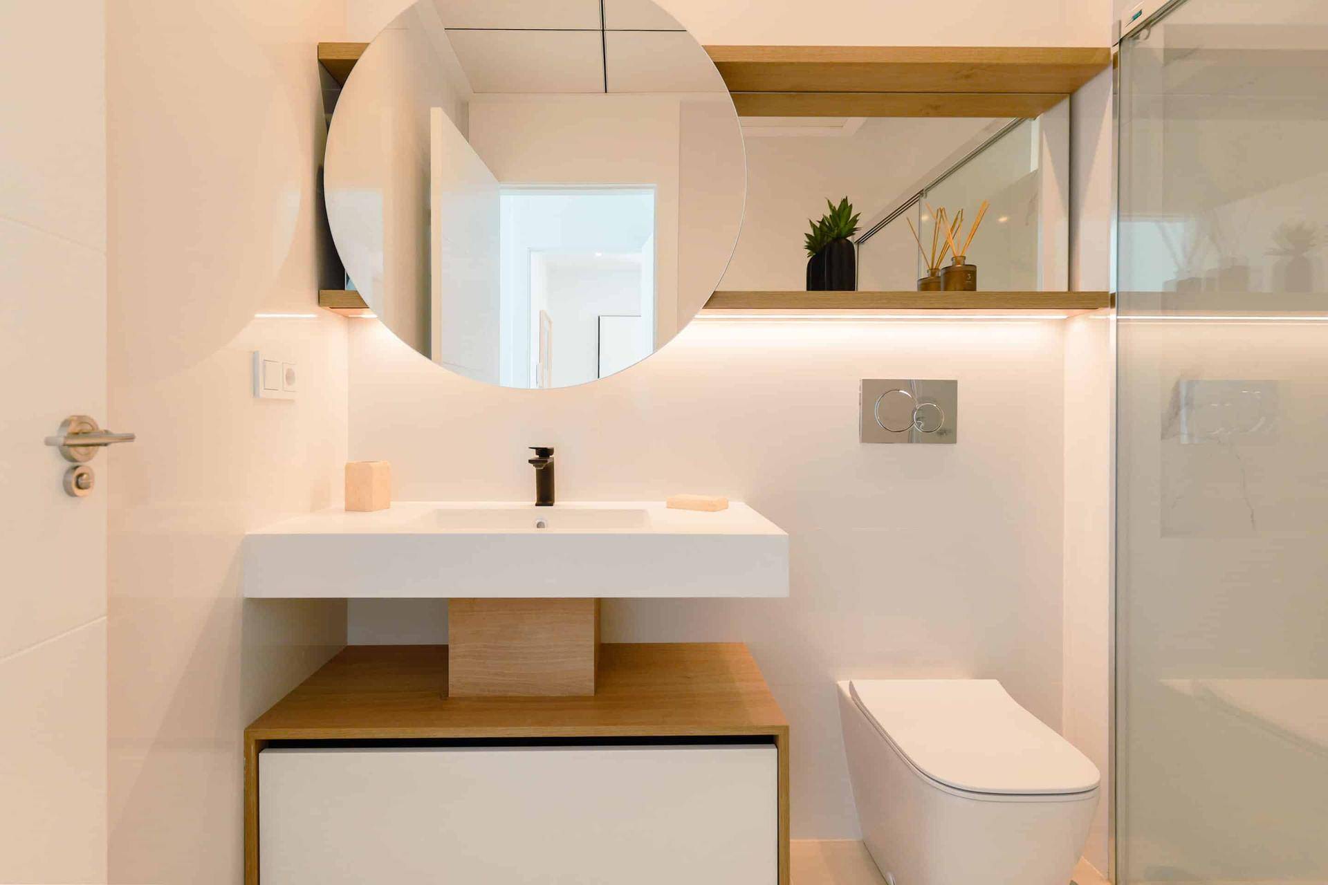 Elegantes Badezimmer mit modernem Waschtisch, rundem Spiegel und integrierter Beleuchtung.