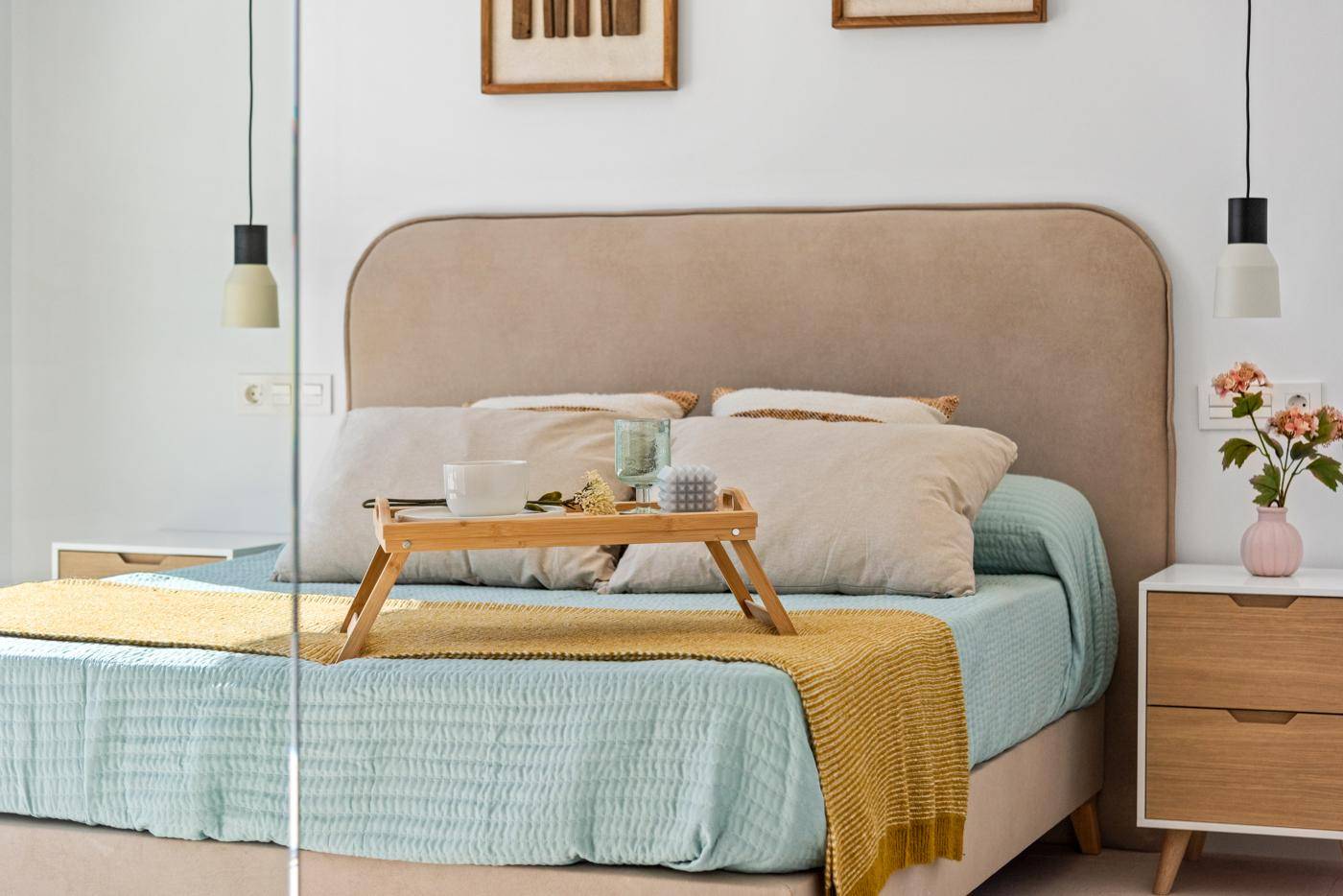 Komfortables Bett mit beigem Kopfteil und dekorativem Tablett in einem hellen Schlafzimmer.