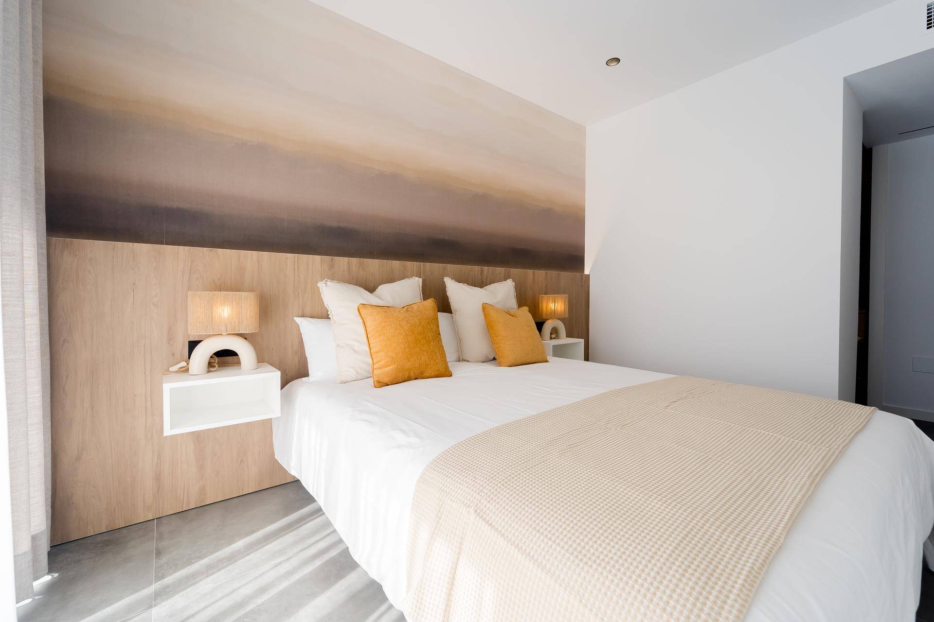 Helles Schlafzimmer mit Doppelbett, Holzkopfteil und stilvoller Wandgestaltung.