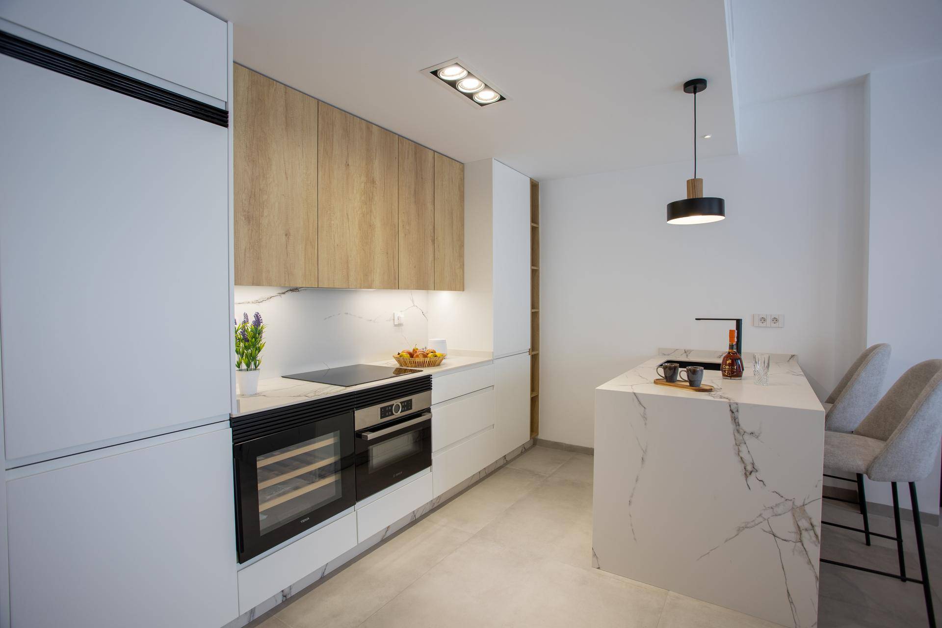 Moderne Einbauküche mit weißen und holzfarbenen Fronten, Kochinsel und integrierten Geräten.