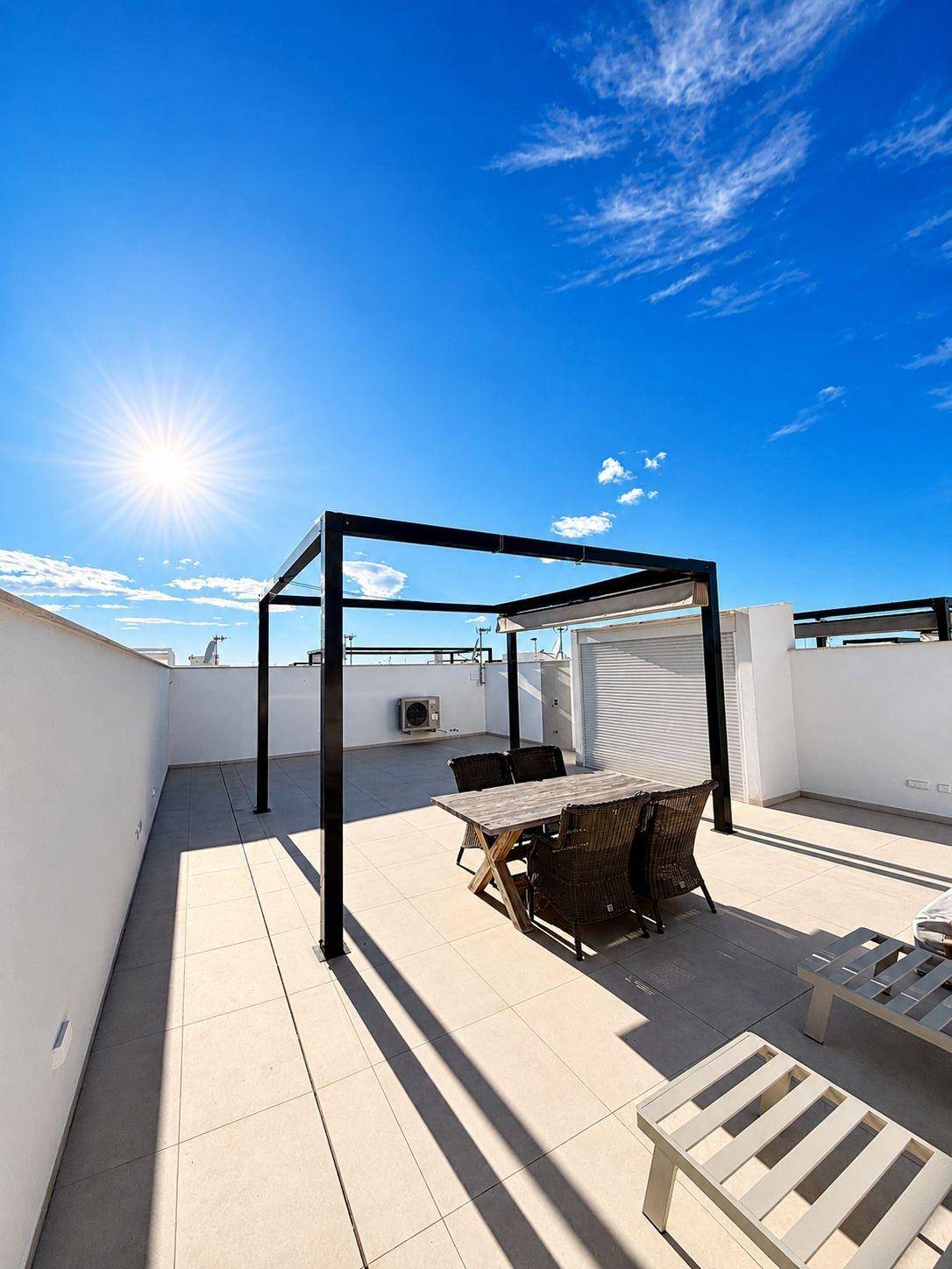 Weitläufige Dachterrasse mit Essbereich unter einer Pergola und viel Sonnenlicht.