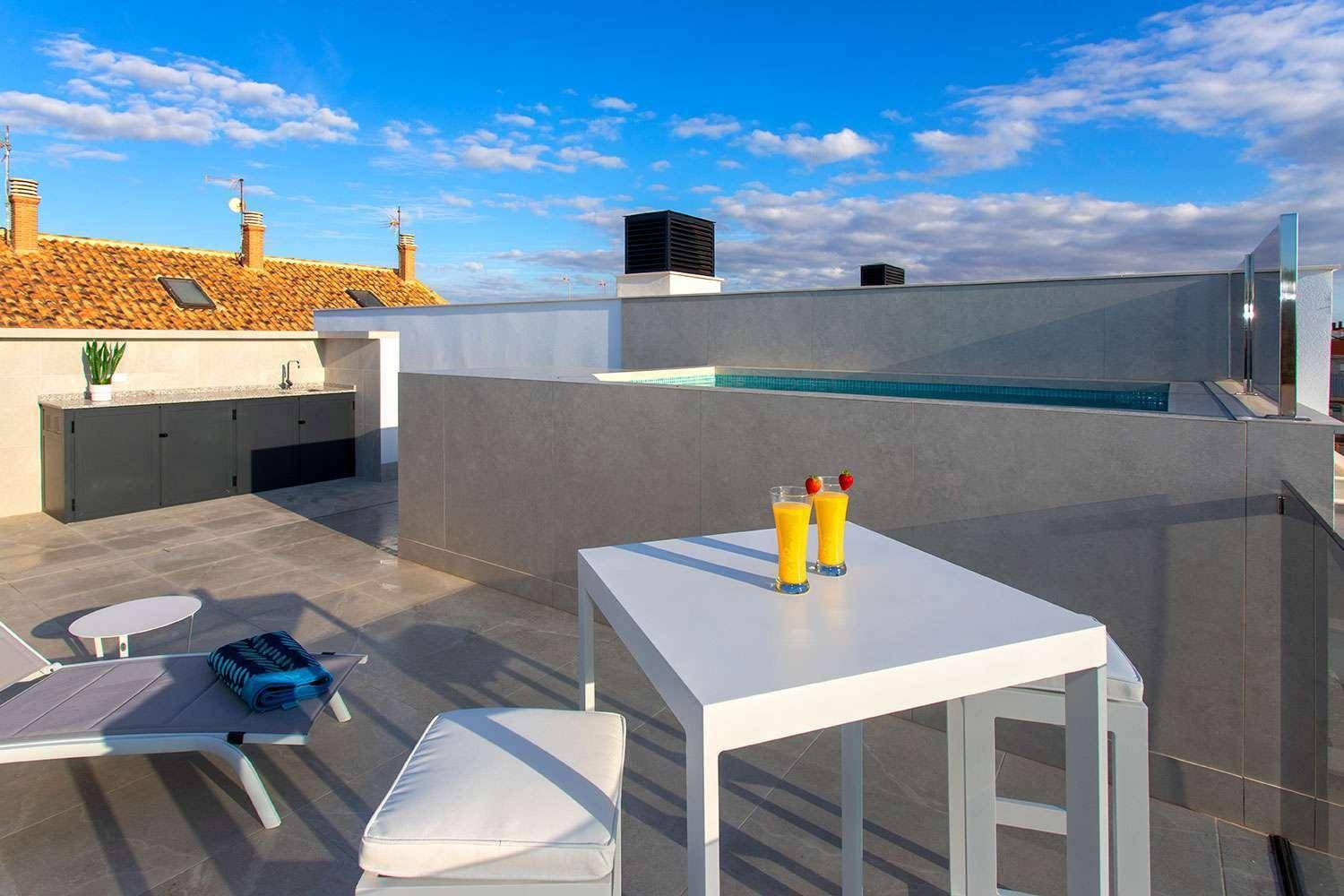 Sonnige Dachterrasse mit kleinem Pool, Außenküche und bequemen Sitzgelegenheiten unter blauem Himmel.